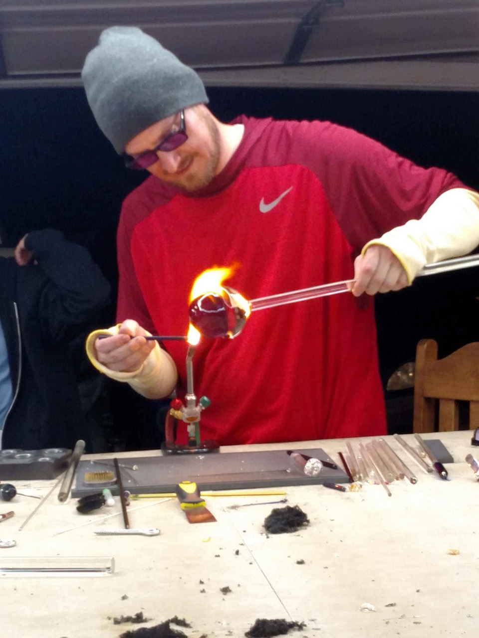 Will Stuckenberg shaping a glowing glass sphere between glass rods above the torch
