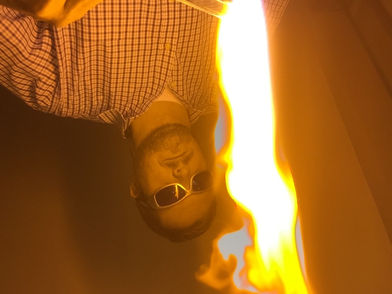 Will Stuckenberg in a checked shirt behind a tall orange torch flame