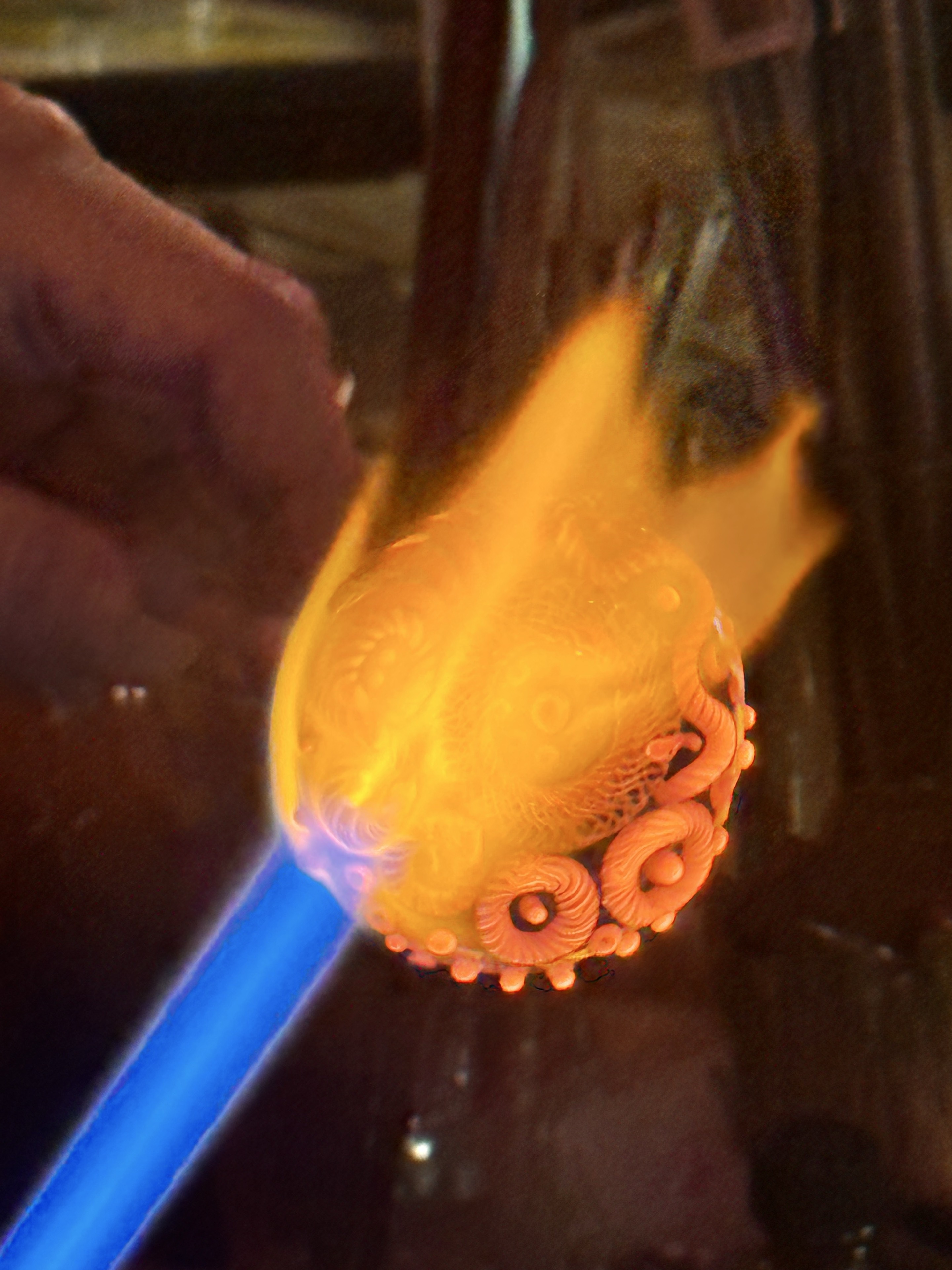 Close view of patterned glass with raised circular details glowing orange in the torch flame