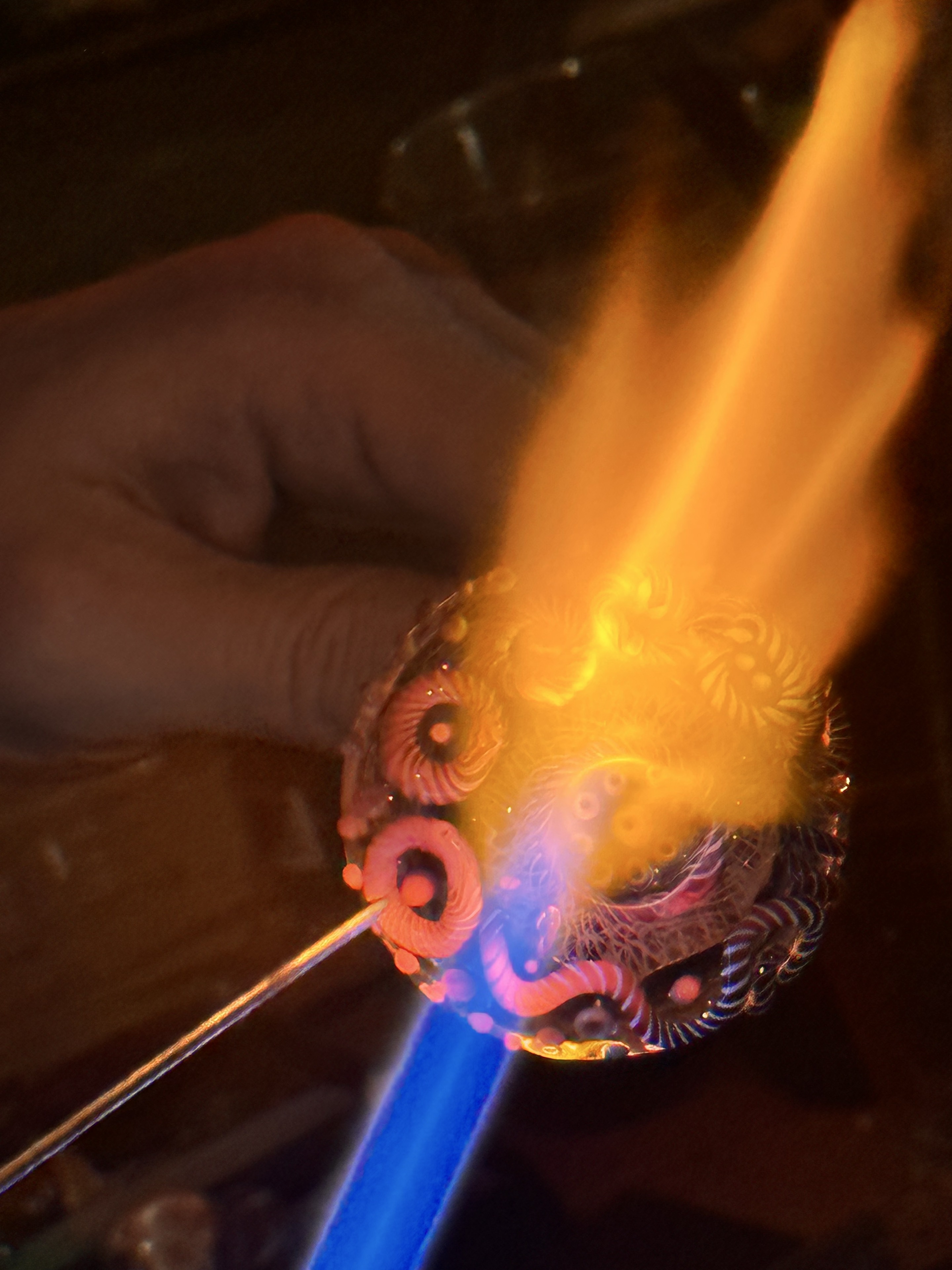 A detailed patterned glass piece turning through the blue and orange flame