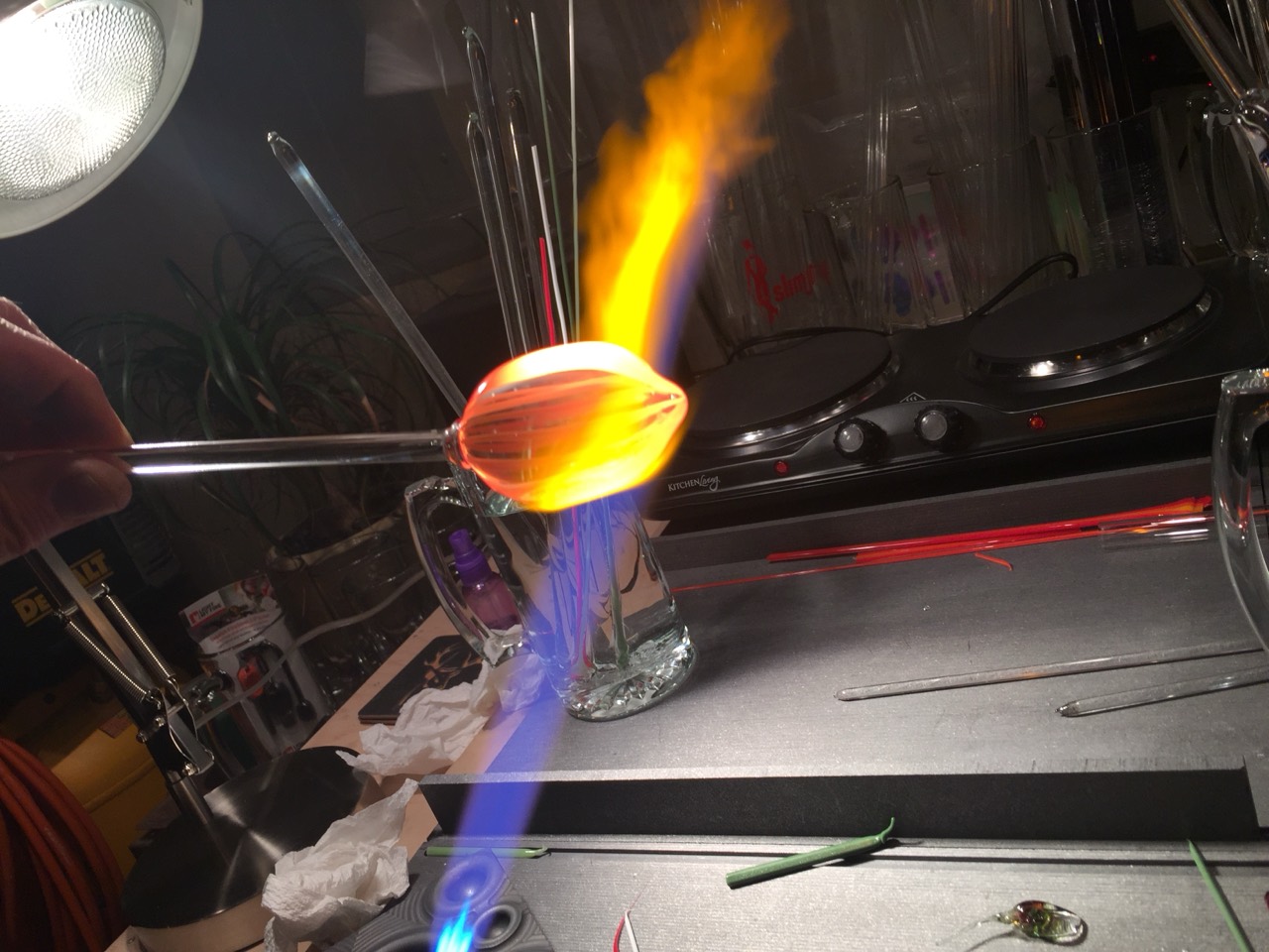A striped glass piece held horizontally in the flame above the workbench