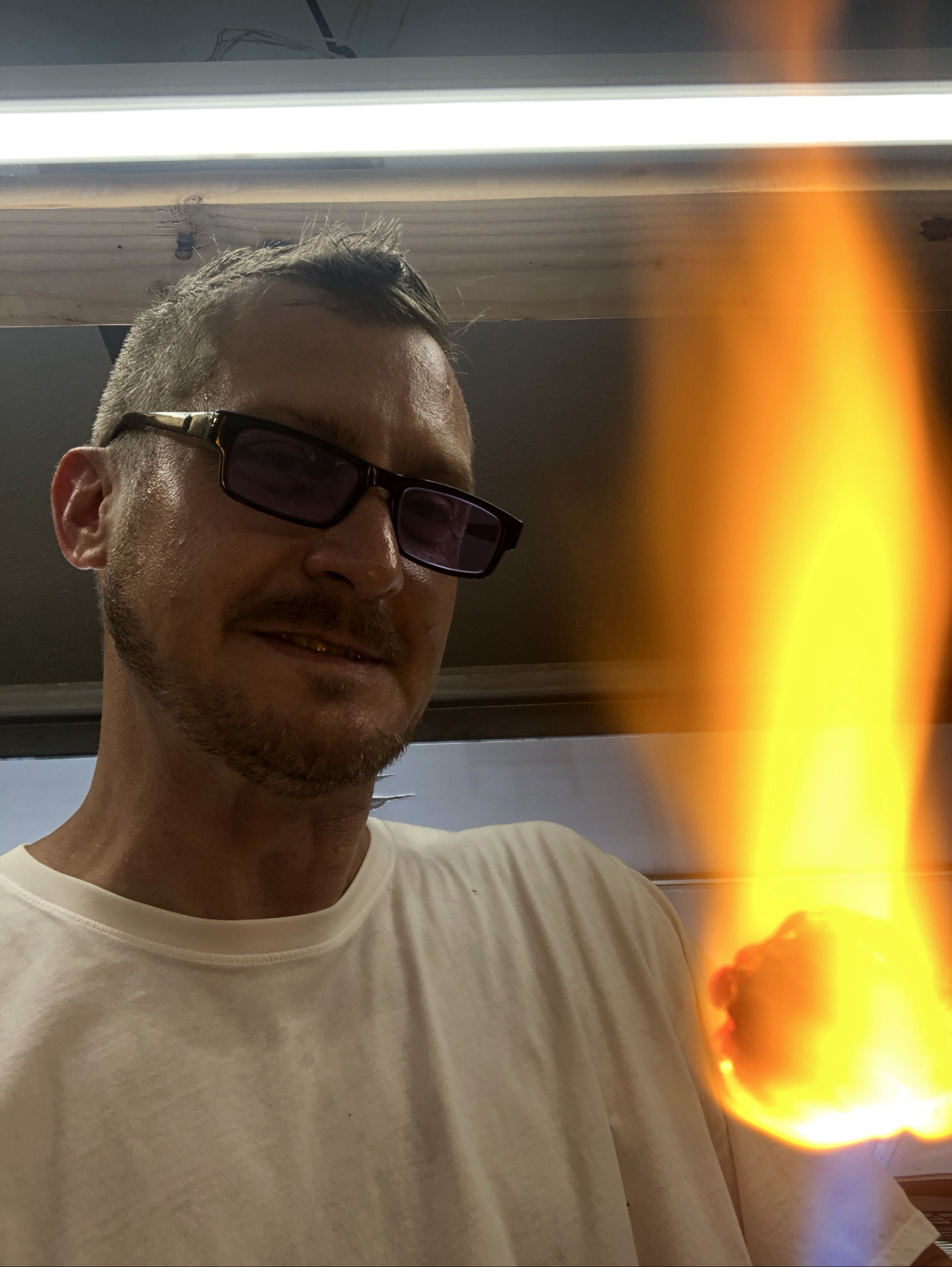 Will Stuckenberg in a white shirt beside a bright orange flame and glowing glass