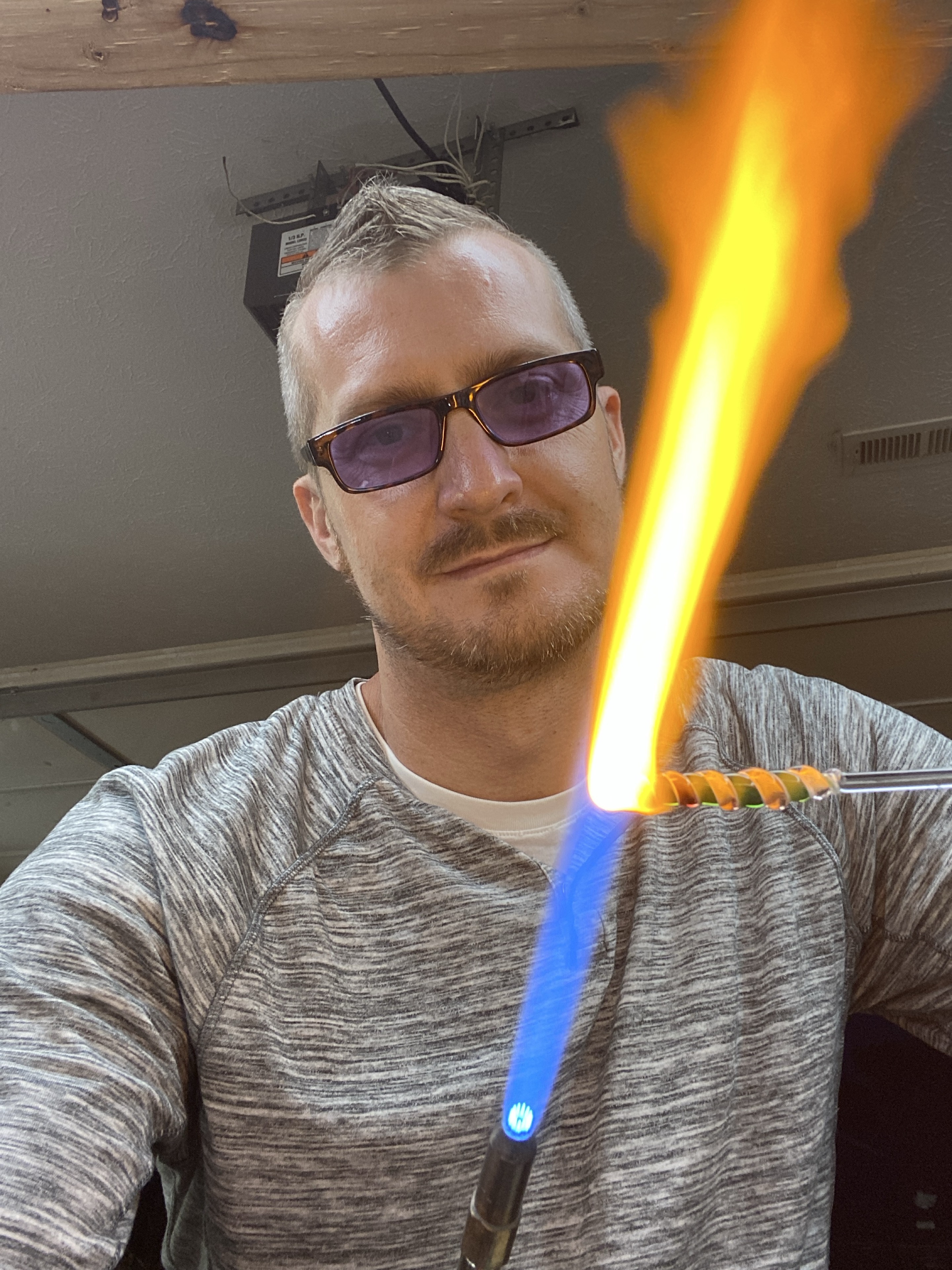 Will Stuckenberg in a gray shirt heating glass with orange and green spiral details