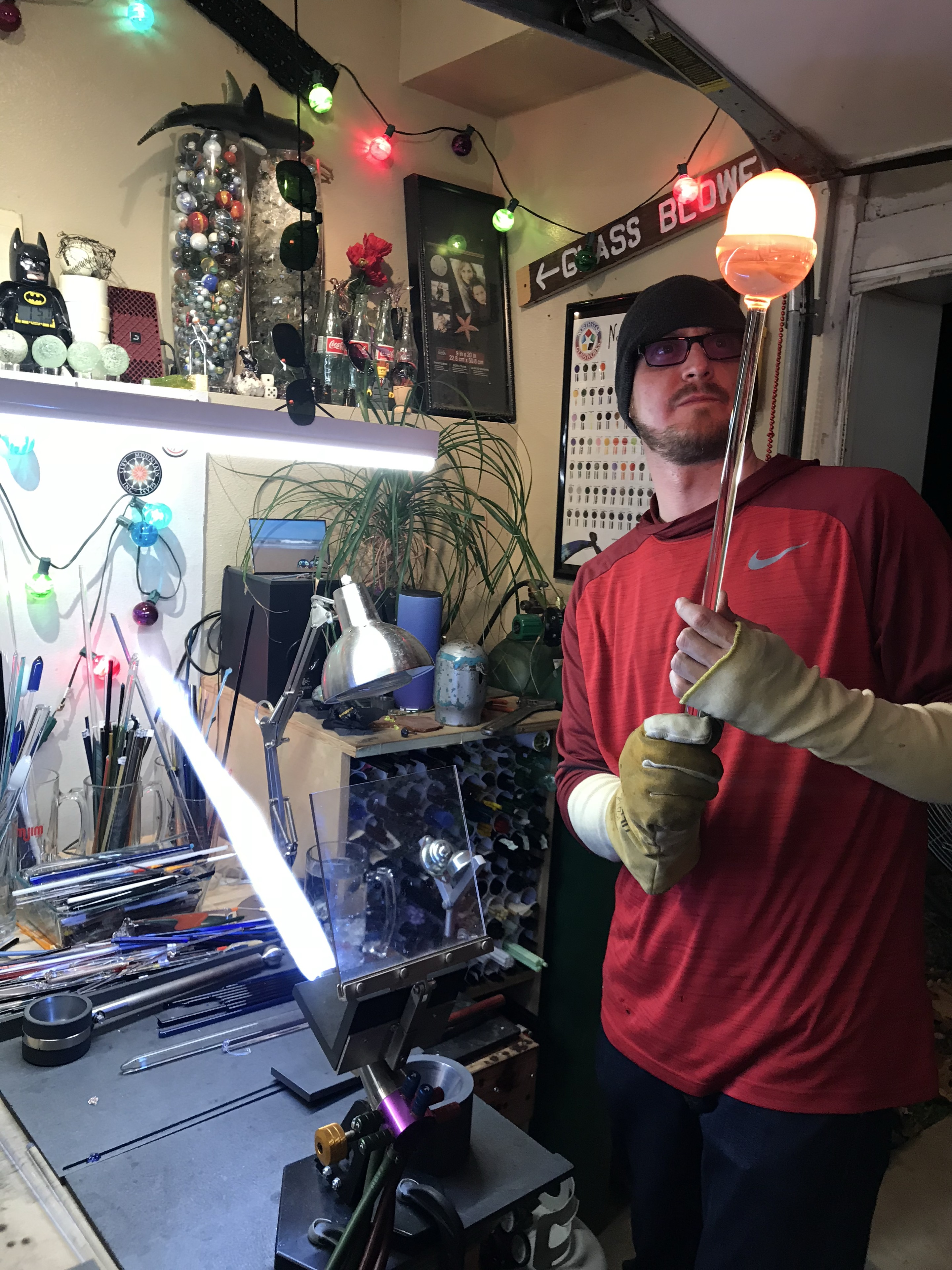 Will Stuckenberg holding glowing glass on a rod at his studio workbench
