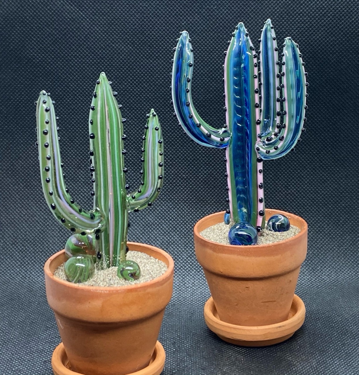 Two glass cacti with blue, green and pink layers, black glass spines and matching marbles in terracotta pots