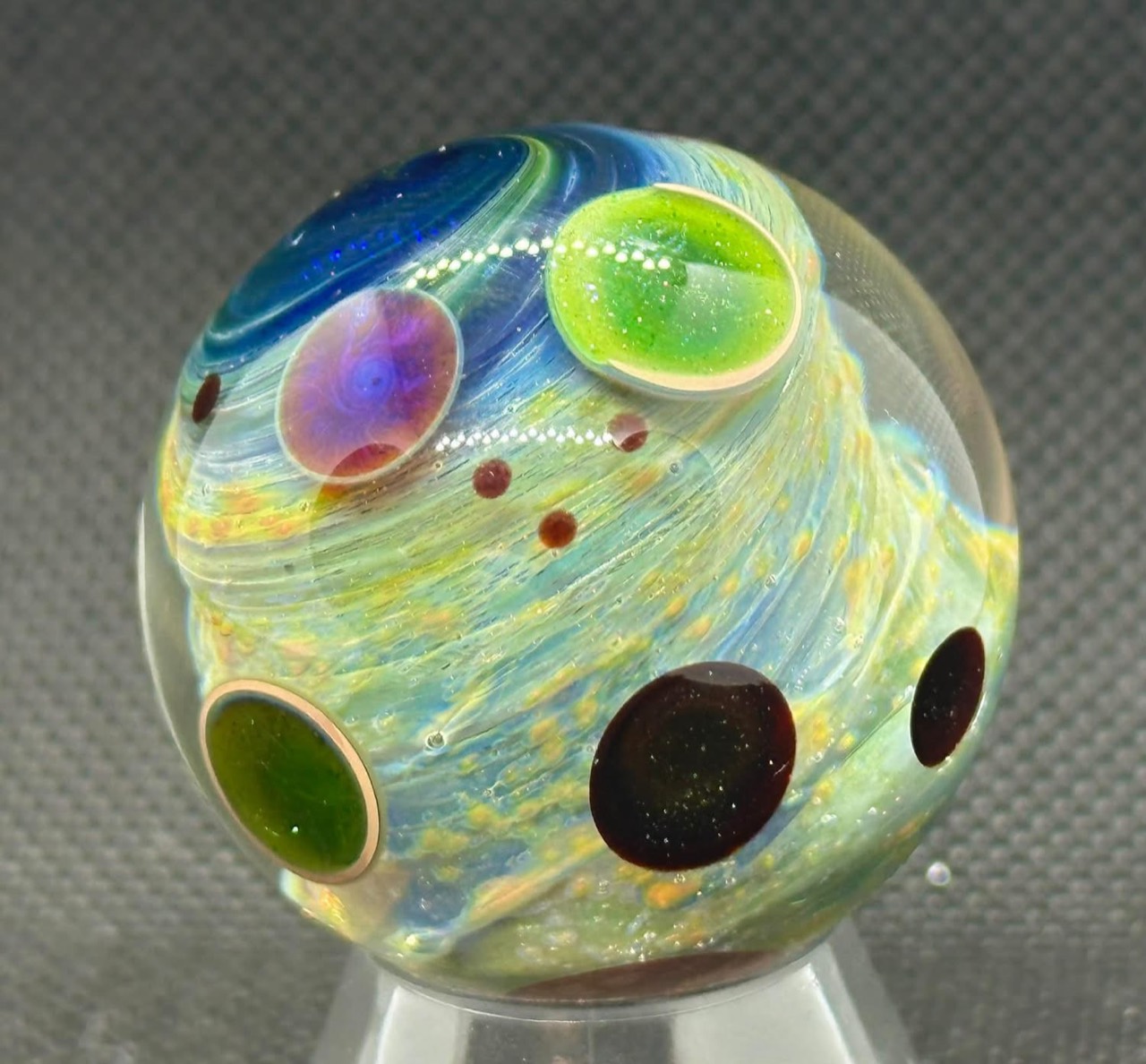 Living Planet marble showing pale blue and golden currents wrapping around colored circular forms