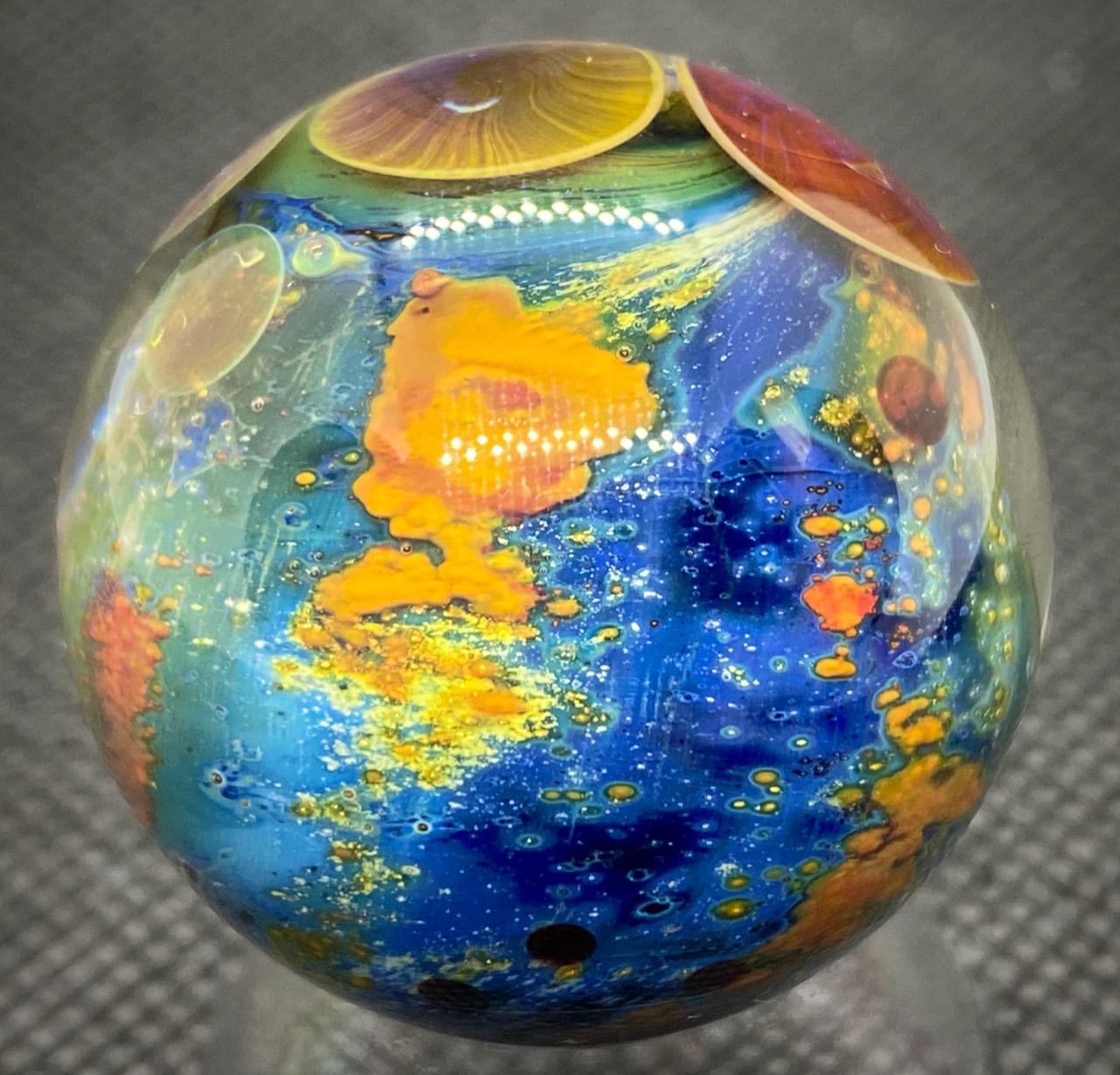 Planet Series marble with blue and green glass, orange detail, and yellow and purple planet-like forms