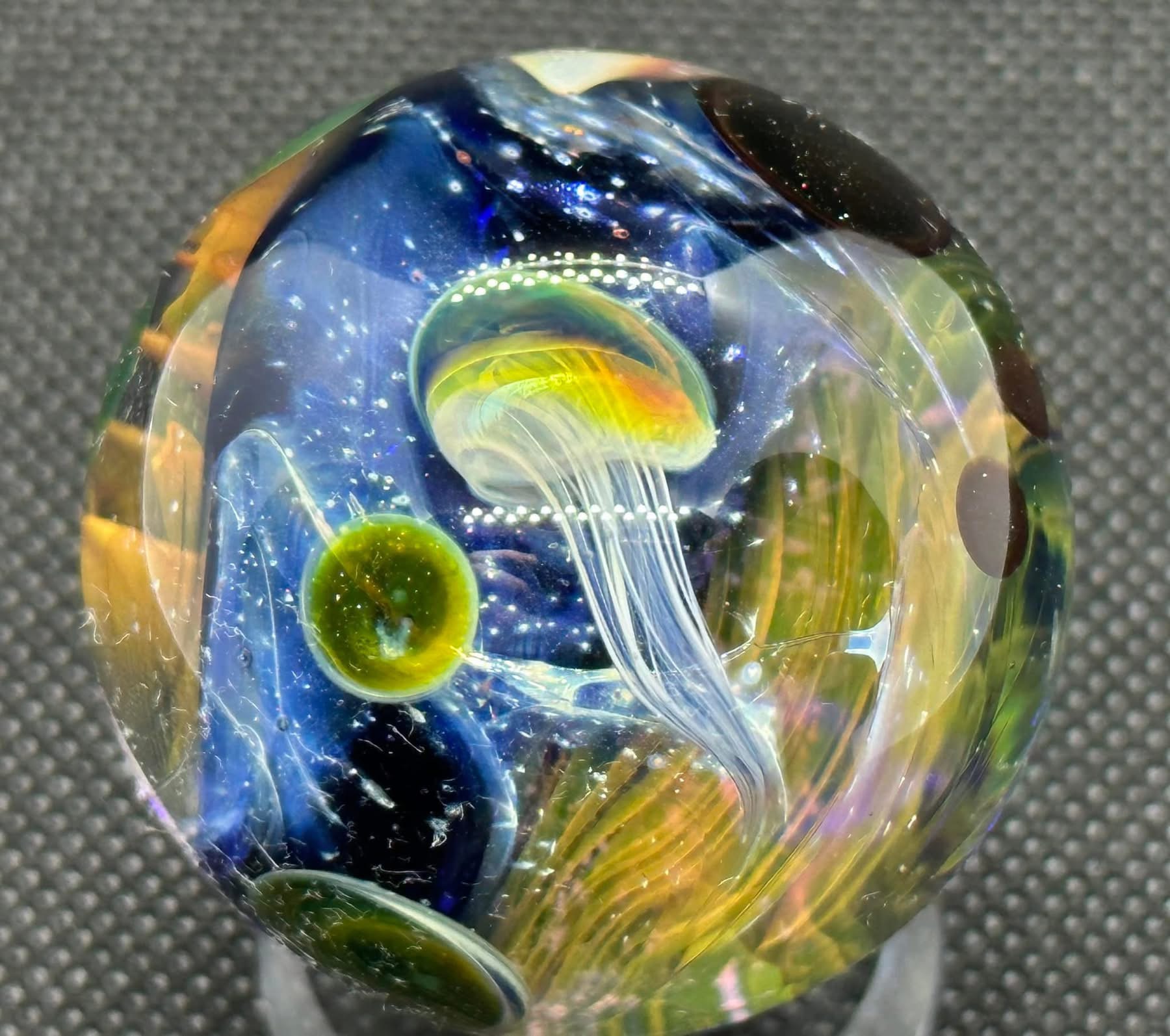 A luminous yellow and green jellyfish with fine white tendrils suspended in deep blue glass