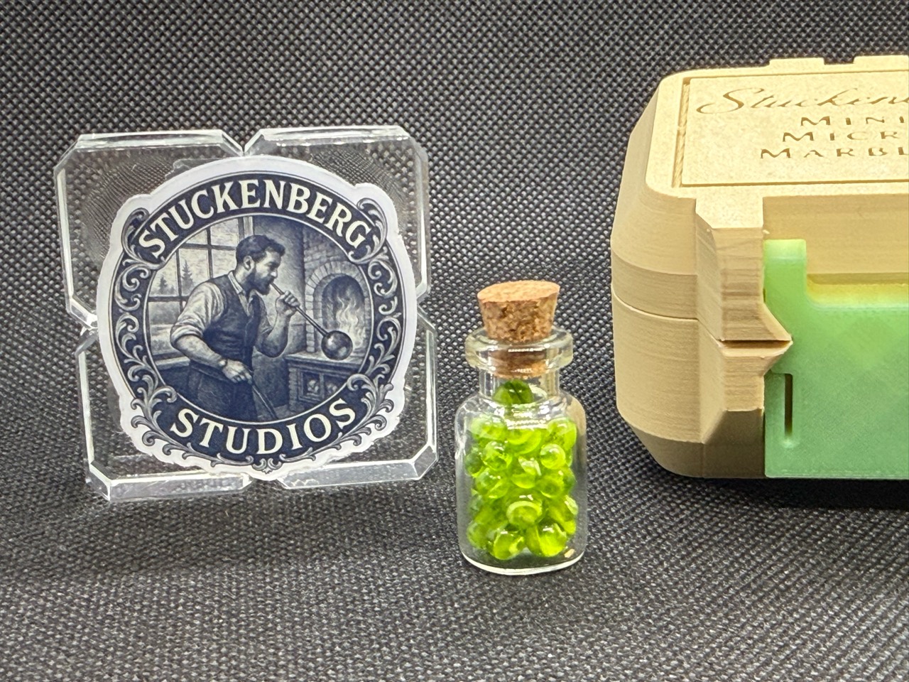 Neon Green Micro Marbles in a corked jar beside the studio logo and a cream case with a green latch