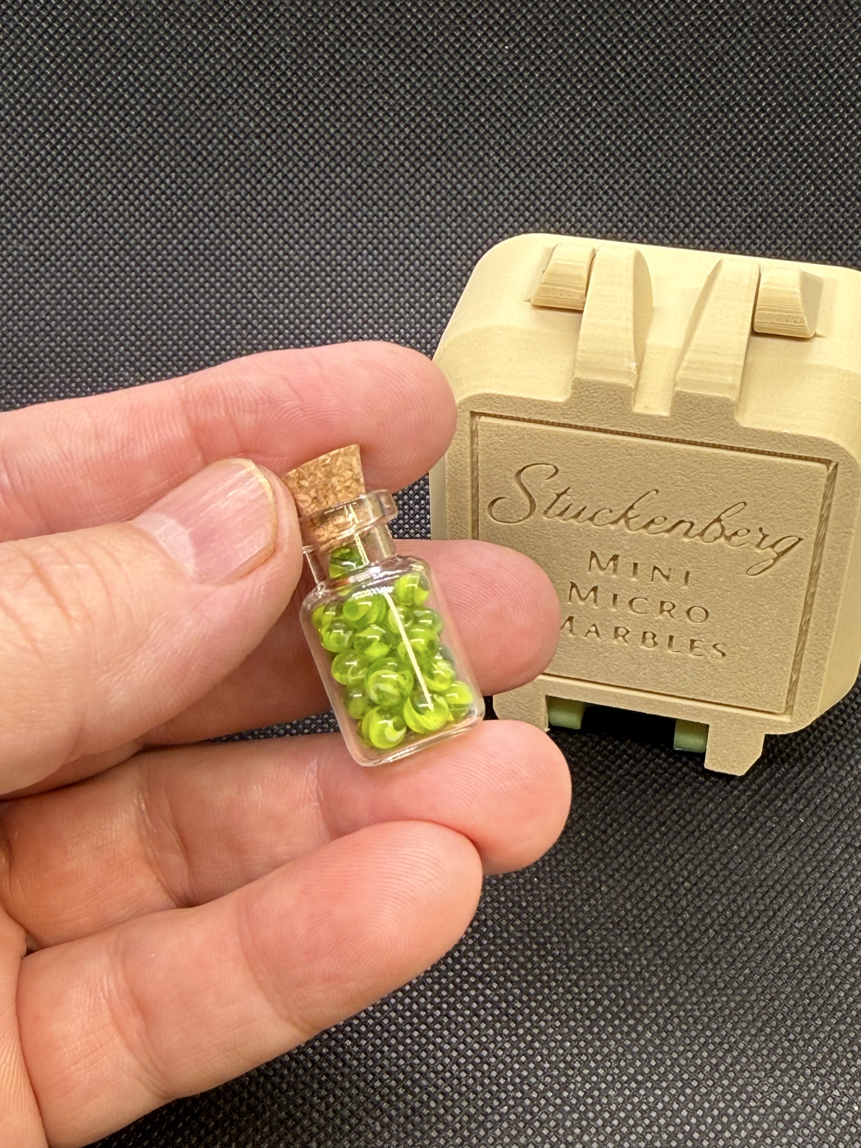 An extra-large jar of Neon Green Micro Marbles held between fingertips for scale