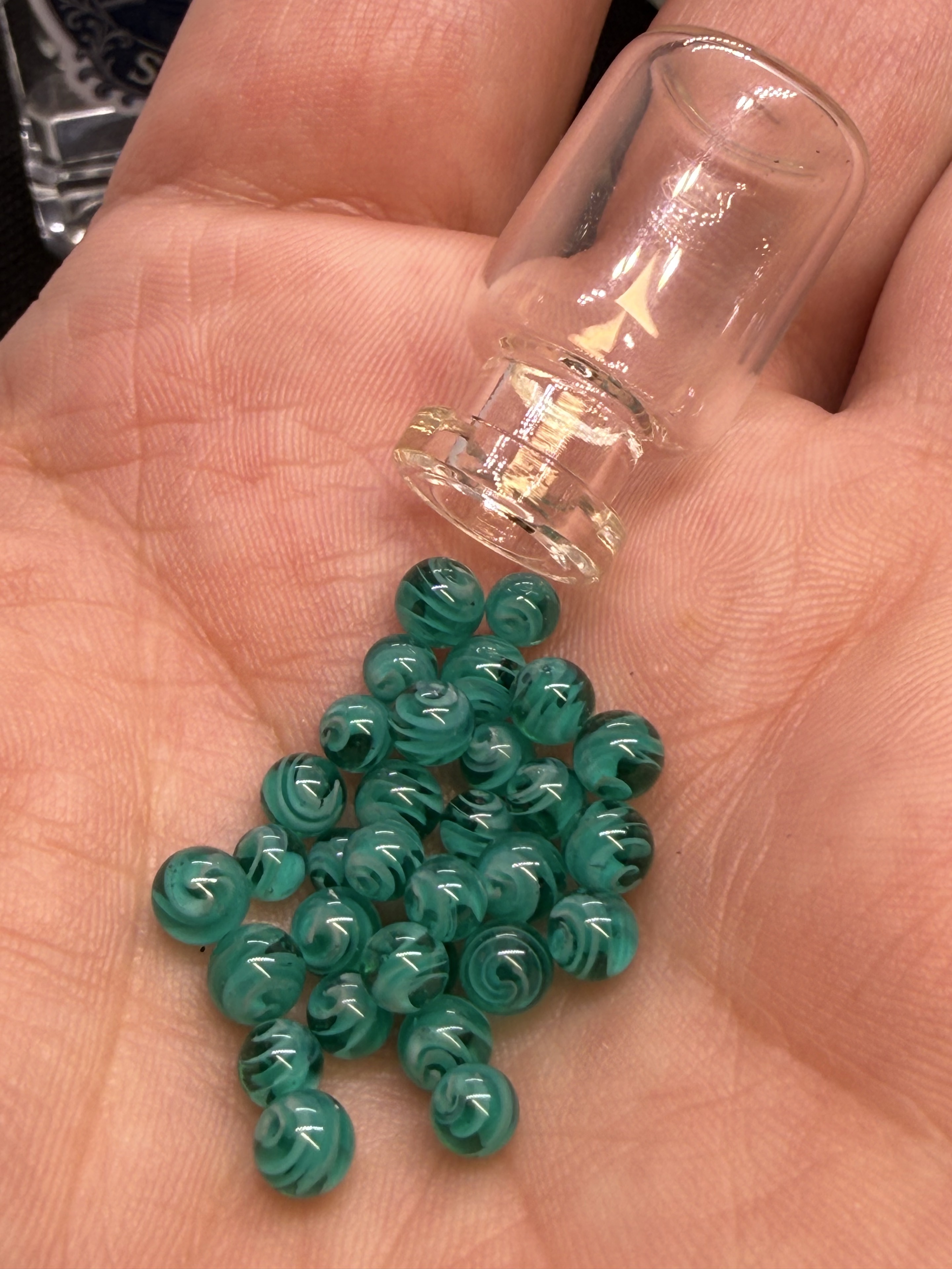 Teal Mini Micro Marbles and a tiny glass bottle in a hand