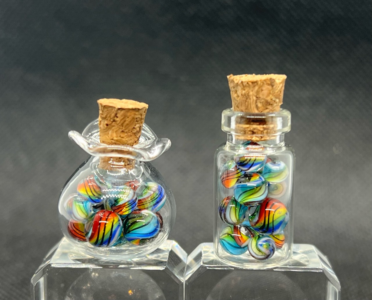 Aqua Rainbow Mini Micro Marbles: Two corked jars of Aqua Rainbow micro marbles displayed on clear blocks