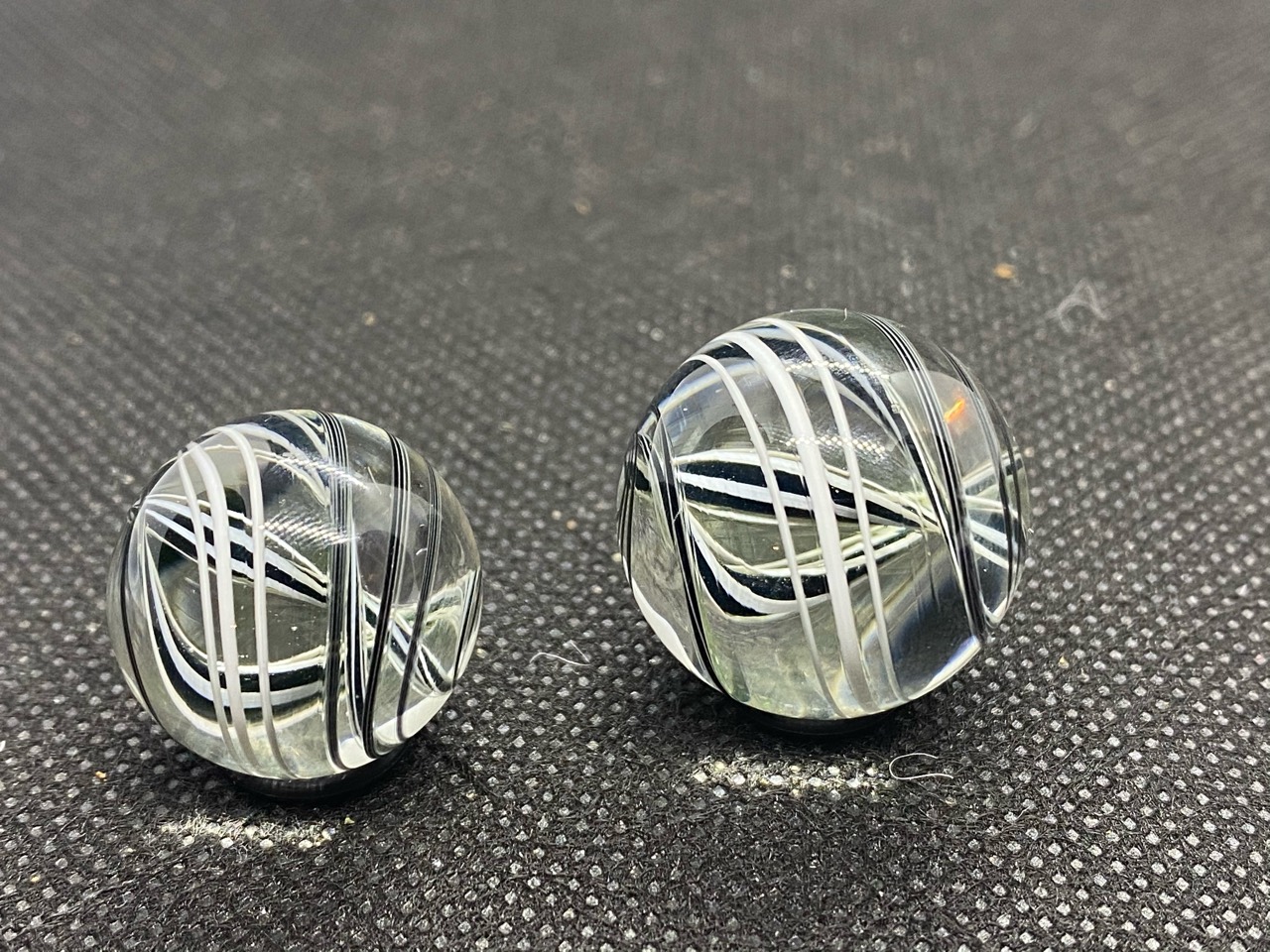 Black & White Spiral Pocket Marble Pair: Normal-light side view of the pair showing white ribbons and fine black lines through clear glass