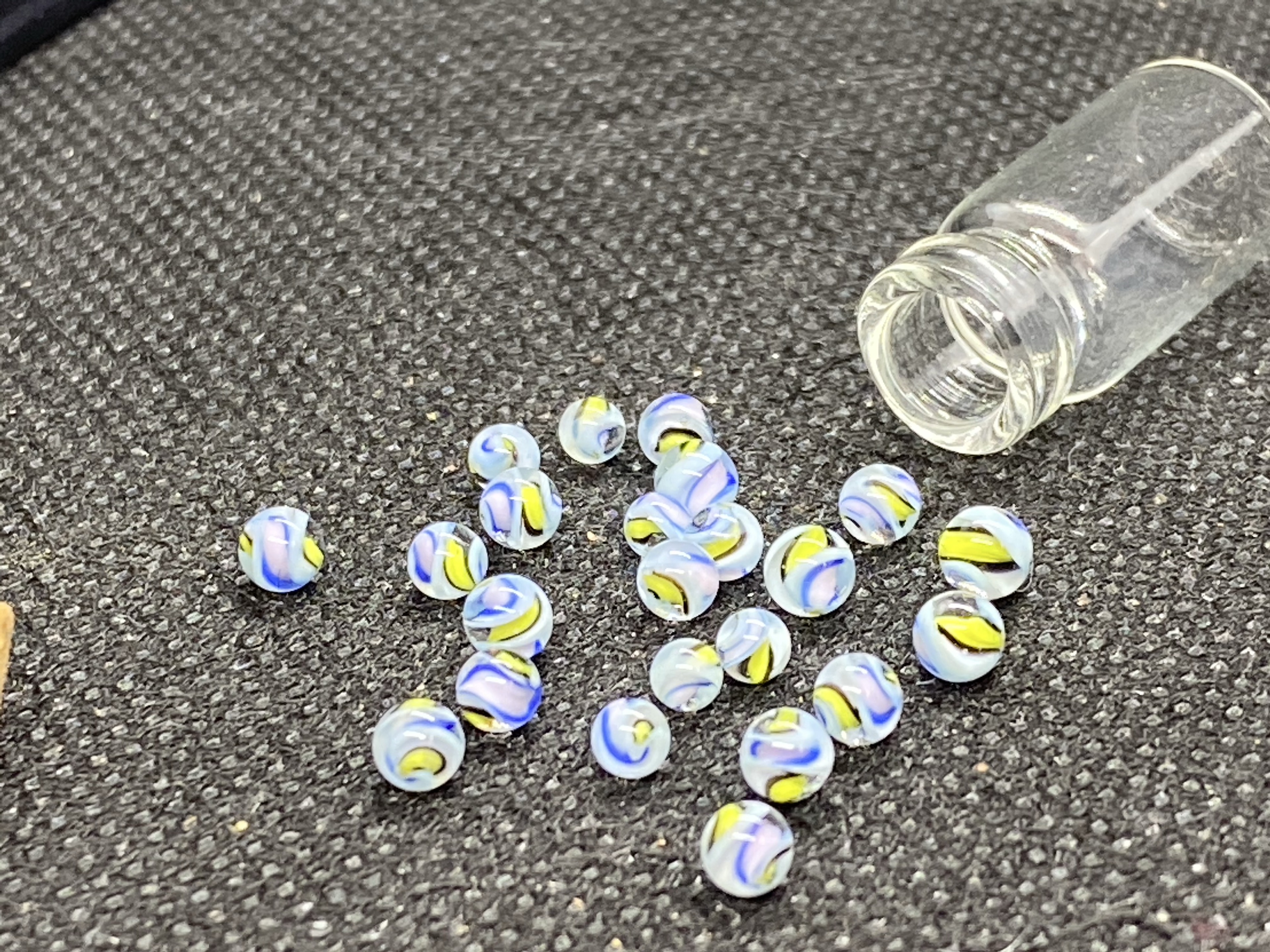 Blue, Lavender & Lemon Mini Micro Marbles: Loose group of pastel ribbon micro marbles beside an open miniature bottle