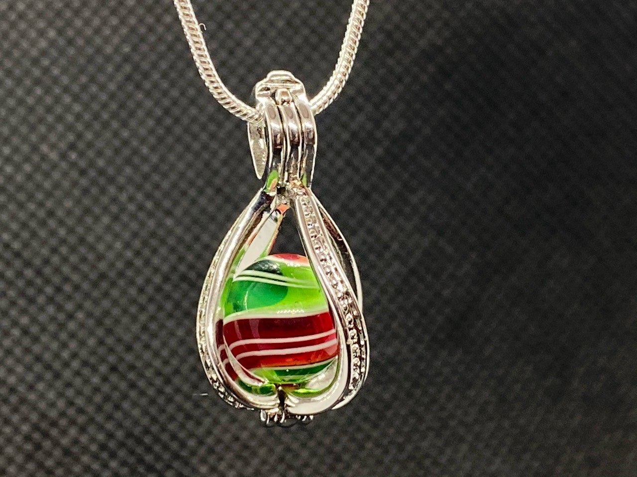 Christmas Pee-wee Marble in a Silver Pearl Cage: Front view of the red, green and white Christmas Pee-wee Marble held in a silver pearl cage pendant