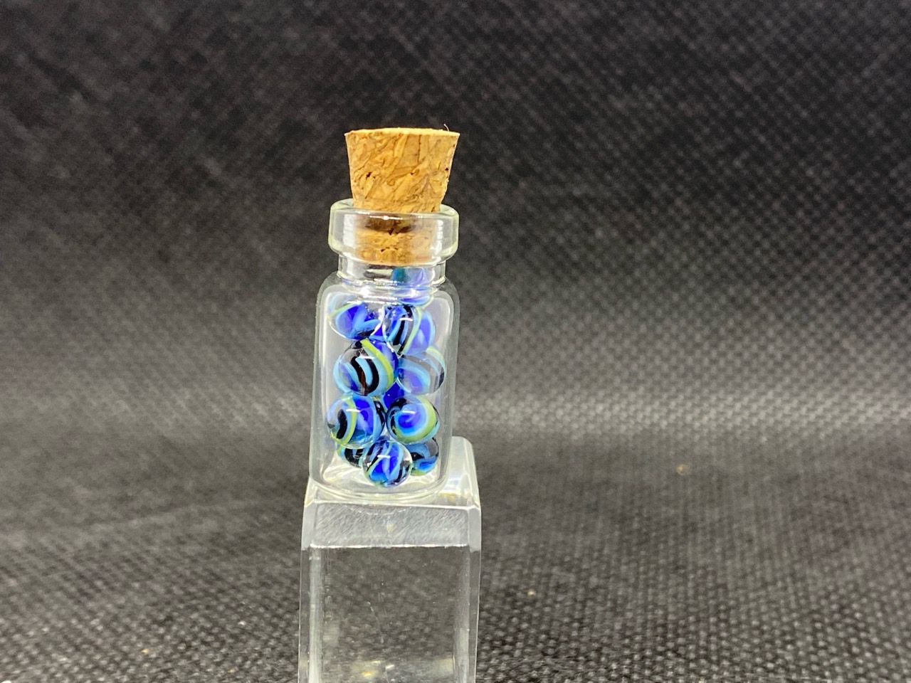 Cobalt & Aqua Ribbon Mini Micro Marbles: Corked miniature bottle filled with cobalt and aqua ribbon micro marbles on a clear block