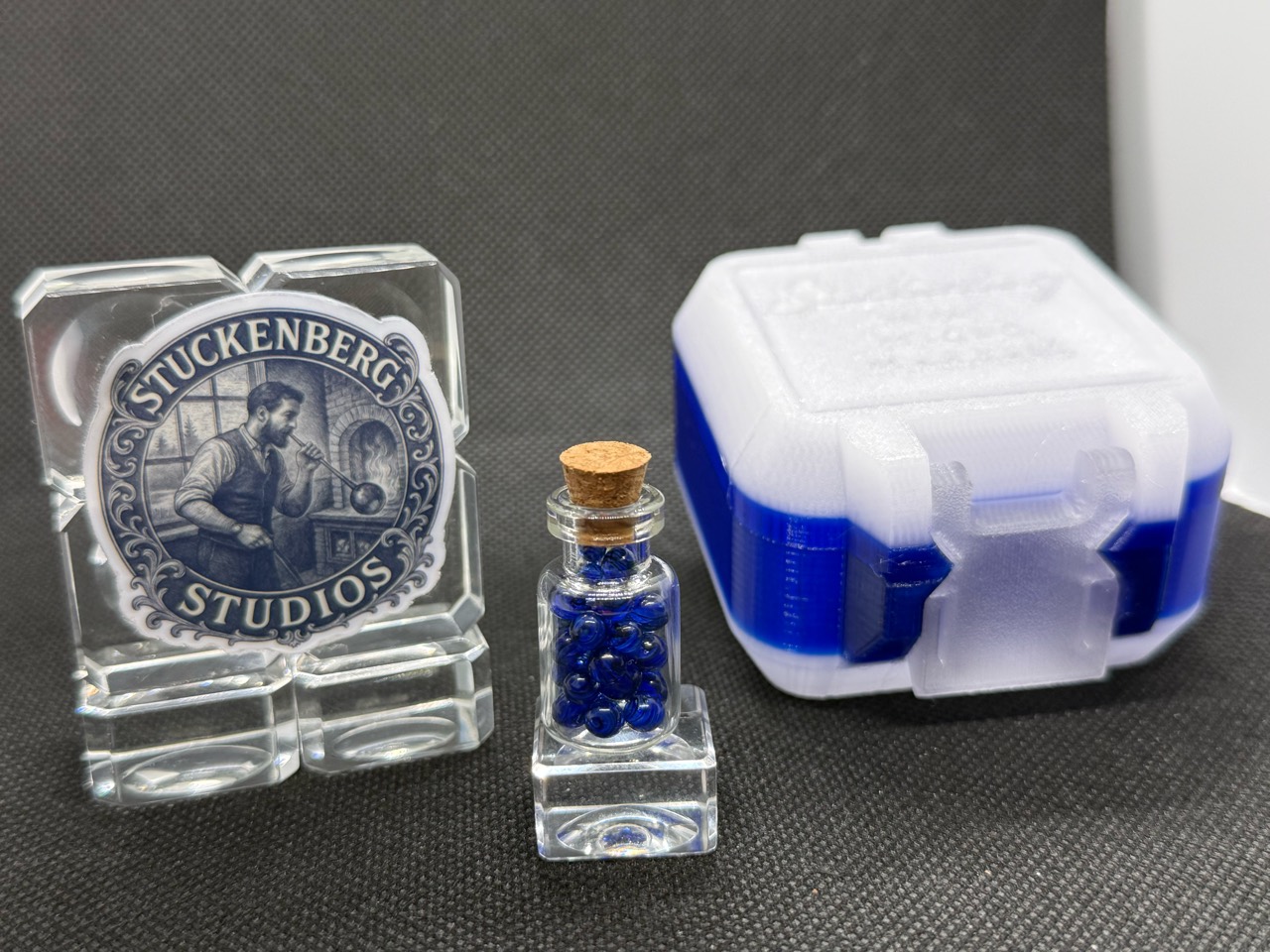 Cobalt UV Uranium Glass Mini Micro Marbles in their jar beside studio branding and a blue-and-white hard case in ordinary light