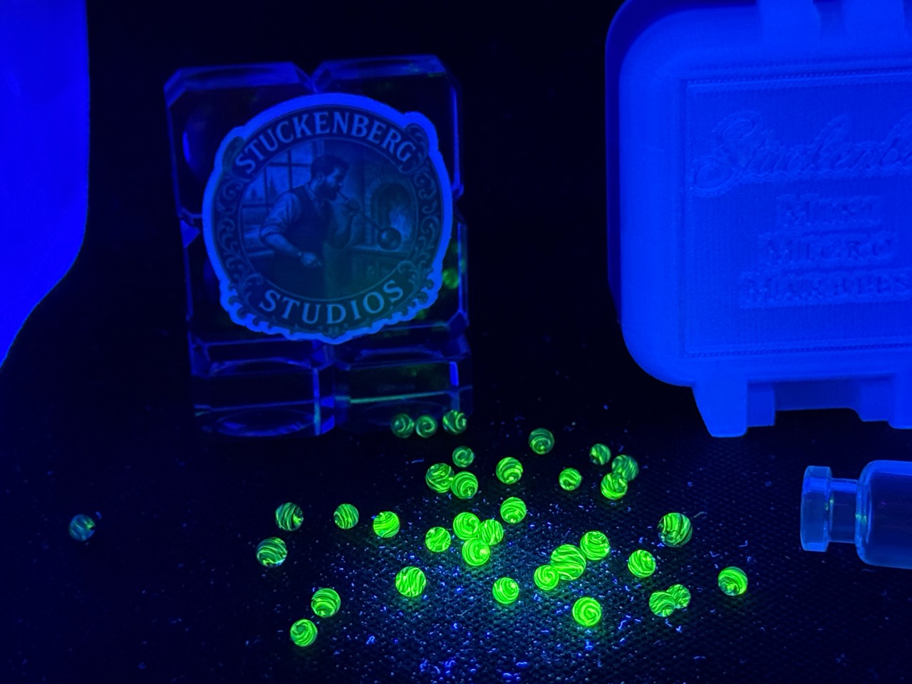 Loose Cobalt UV Uranium Glass Mini Micro Marbles glowing green under UV light beside their jar and hard case