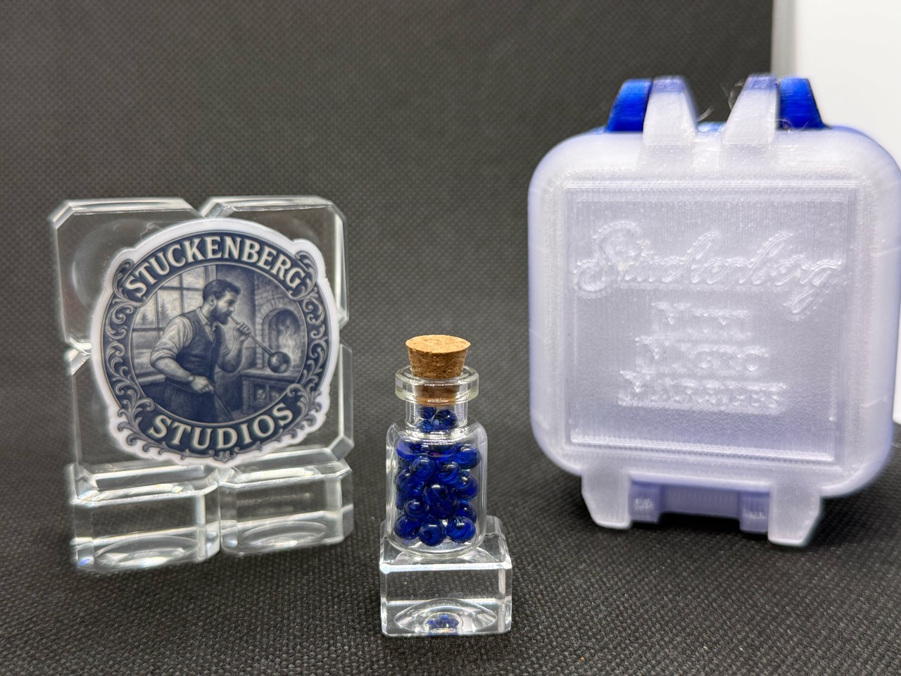 Cobalt UV Uranium Glass Mini Micro Marbles in a corked jar beside a white-and-blue hard case in ordinary light