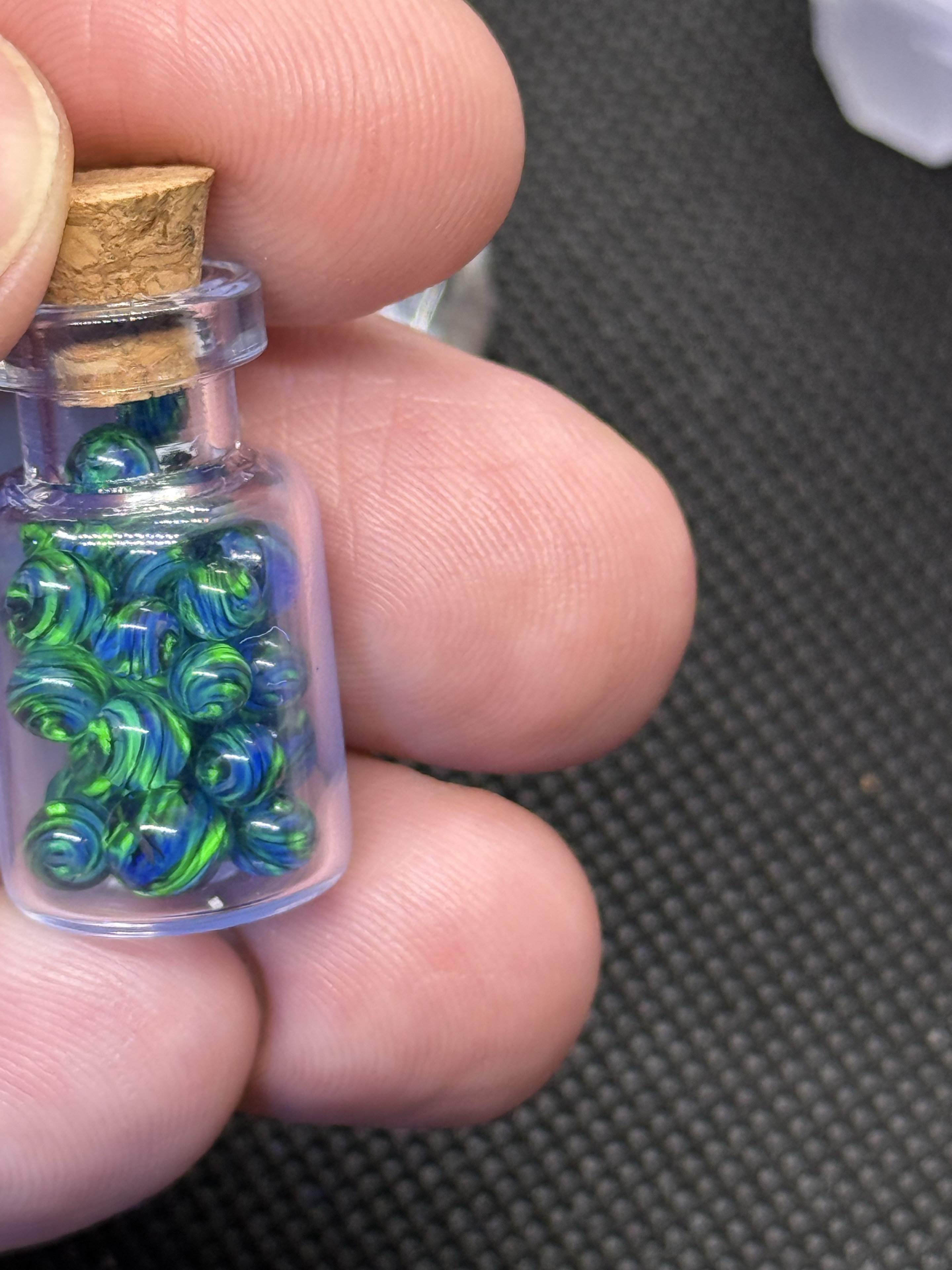 Close view of Cobalt UV Uranium Glass Mini Micro Marbles glowing green in their jar held in hand for scale
