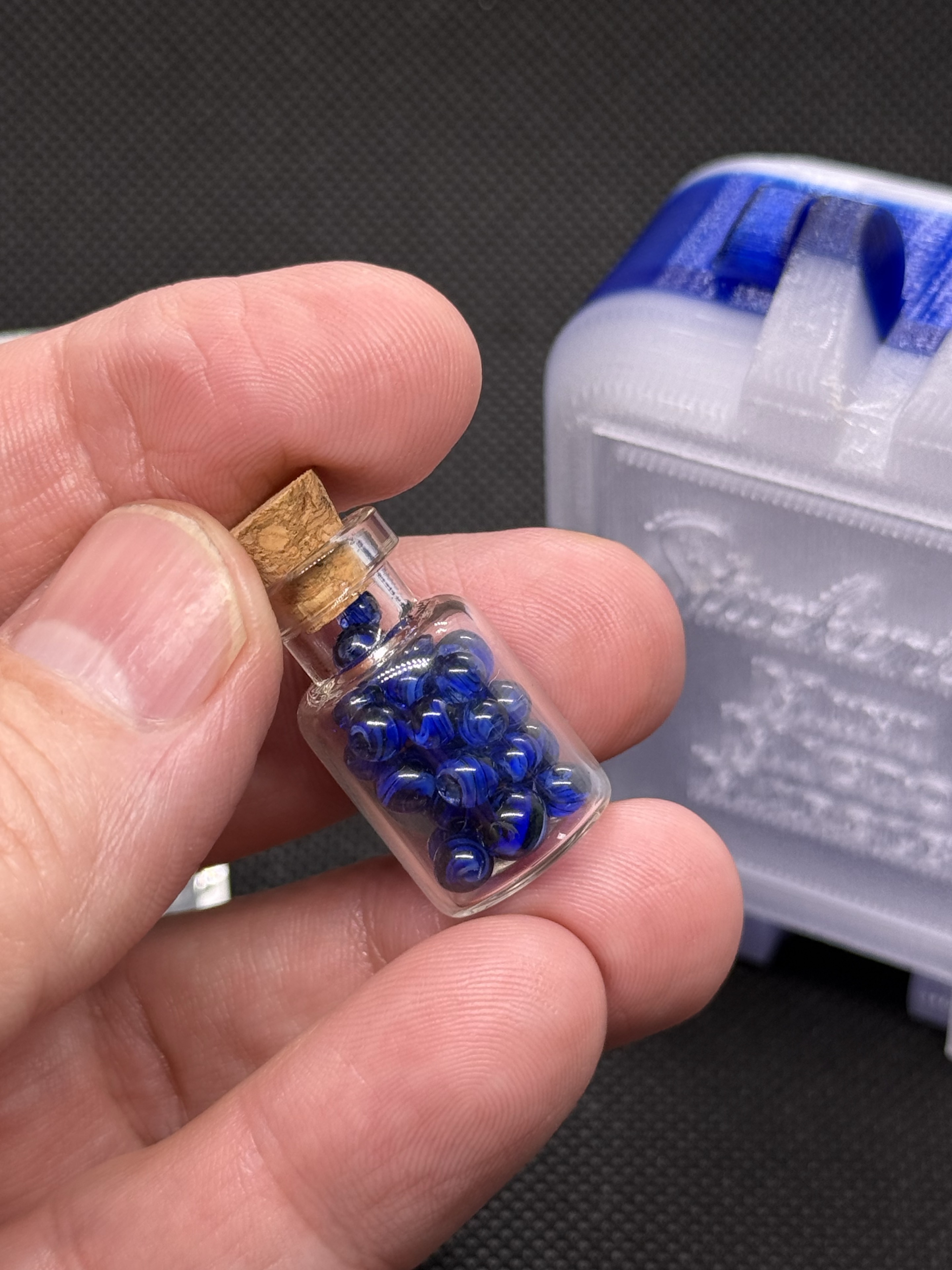 Corked jar of cobalt blue Mini Micro Marbles held in hand for scale in ordinary light