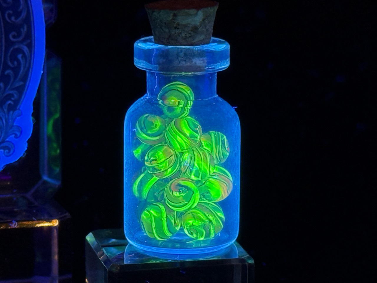 Close view of the bright green UV glow of Electric Rainbow Mini Micro Marbles in their jar