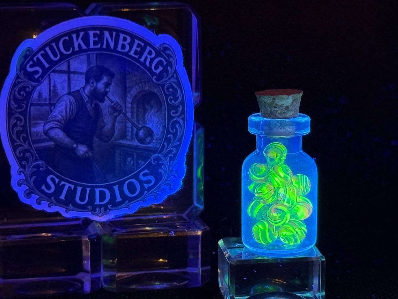 Electric Rainbow Mini Micro Marbles glowing bright green under a black light in their corked jar