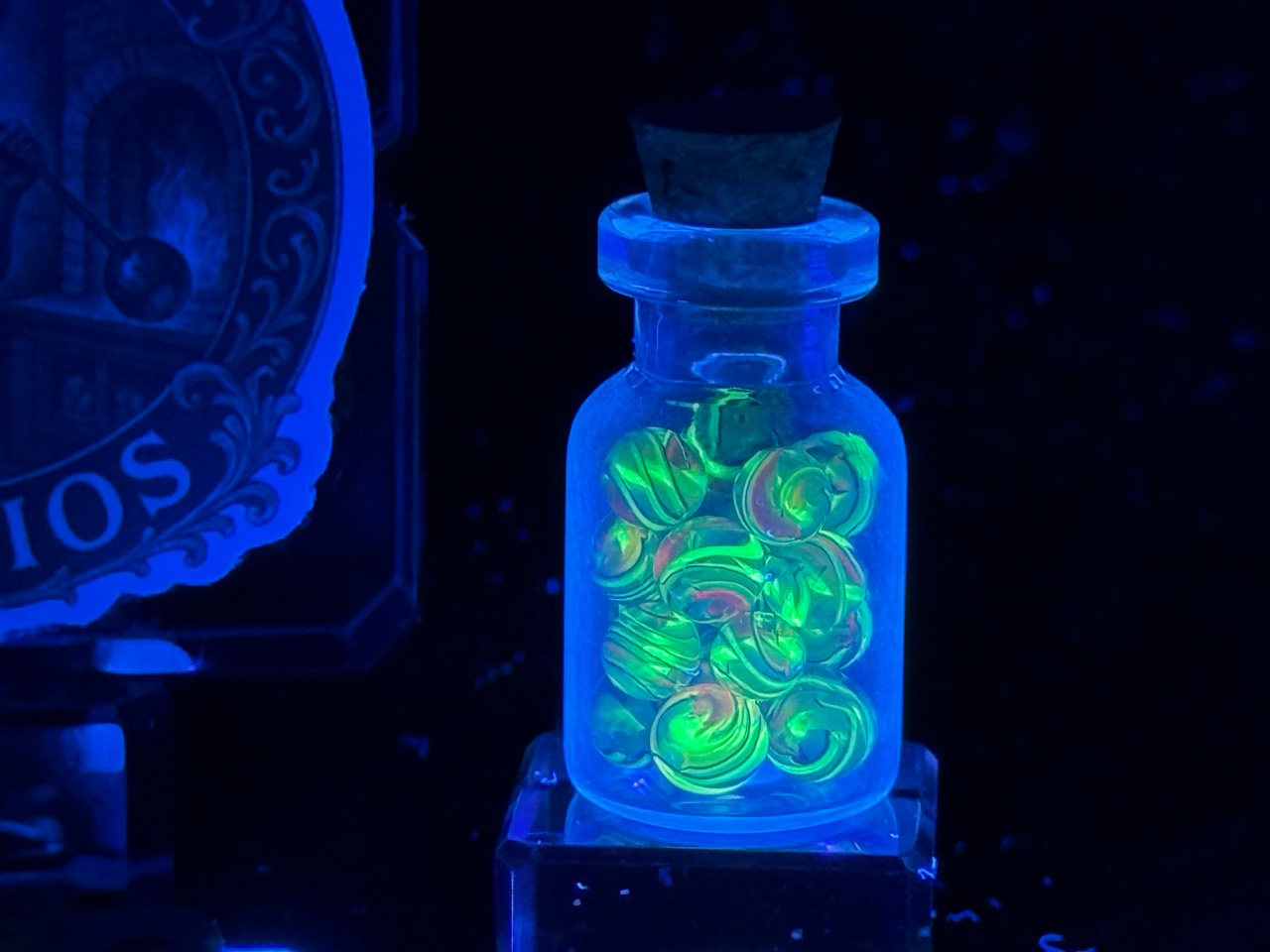 Electric Rainbow Mini Micro Marbles glowing green under UV light in their corked jar