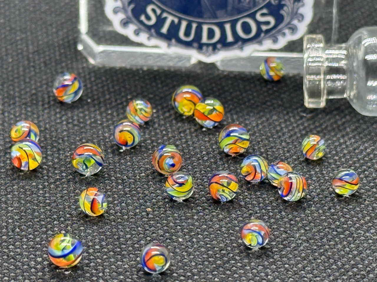 Close view of rainbow ribbons in Electric Rainbow Mini Micro Marbles beside an open jar