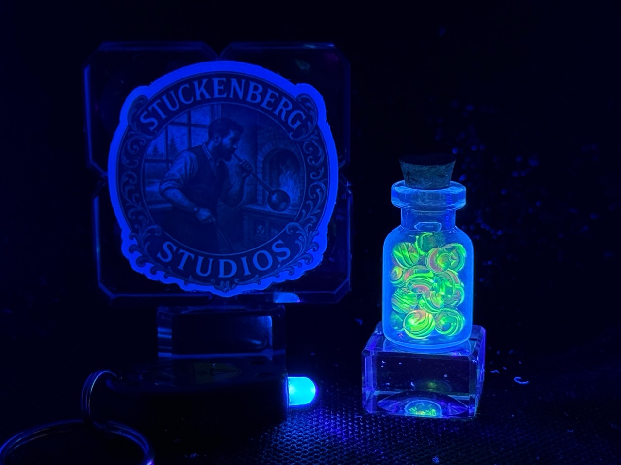 Wide UV view of Electric Rainbow Mini Micro Marbles in their jar with the included black light keychain