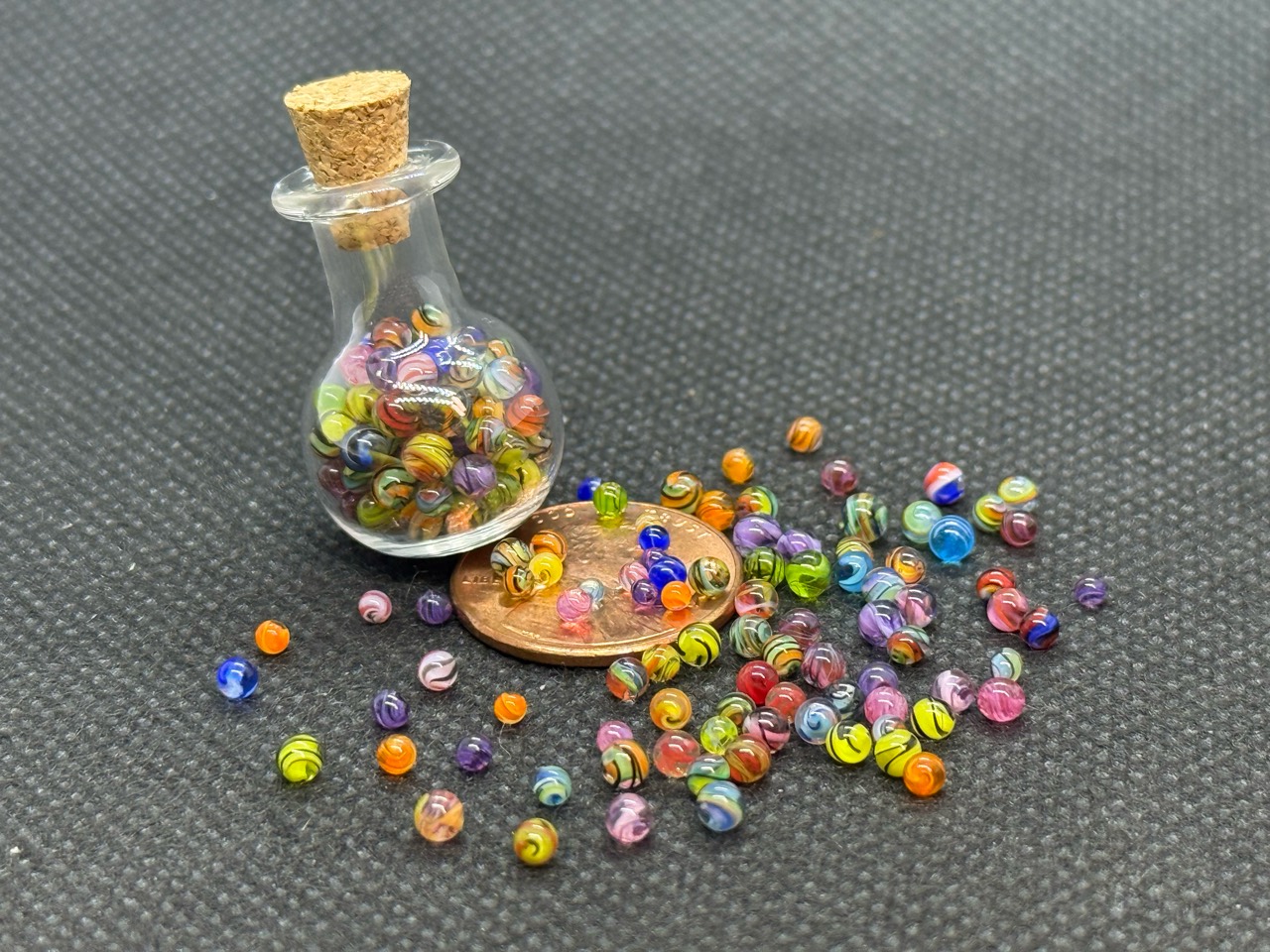 Extra Tiny Mini Micro Marbles: Wider view of the miniature bottle and colorful loose micro marbles around a penny