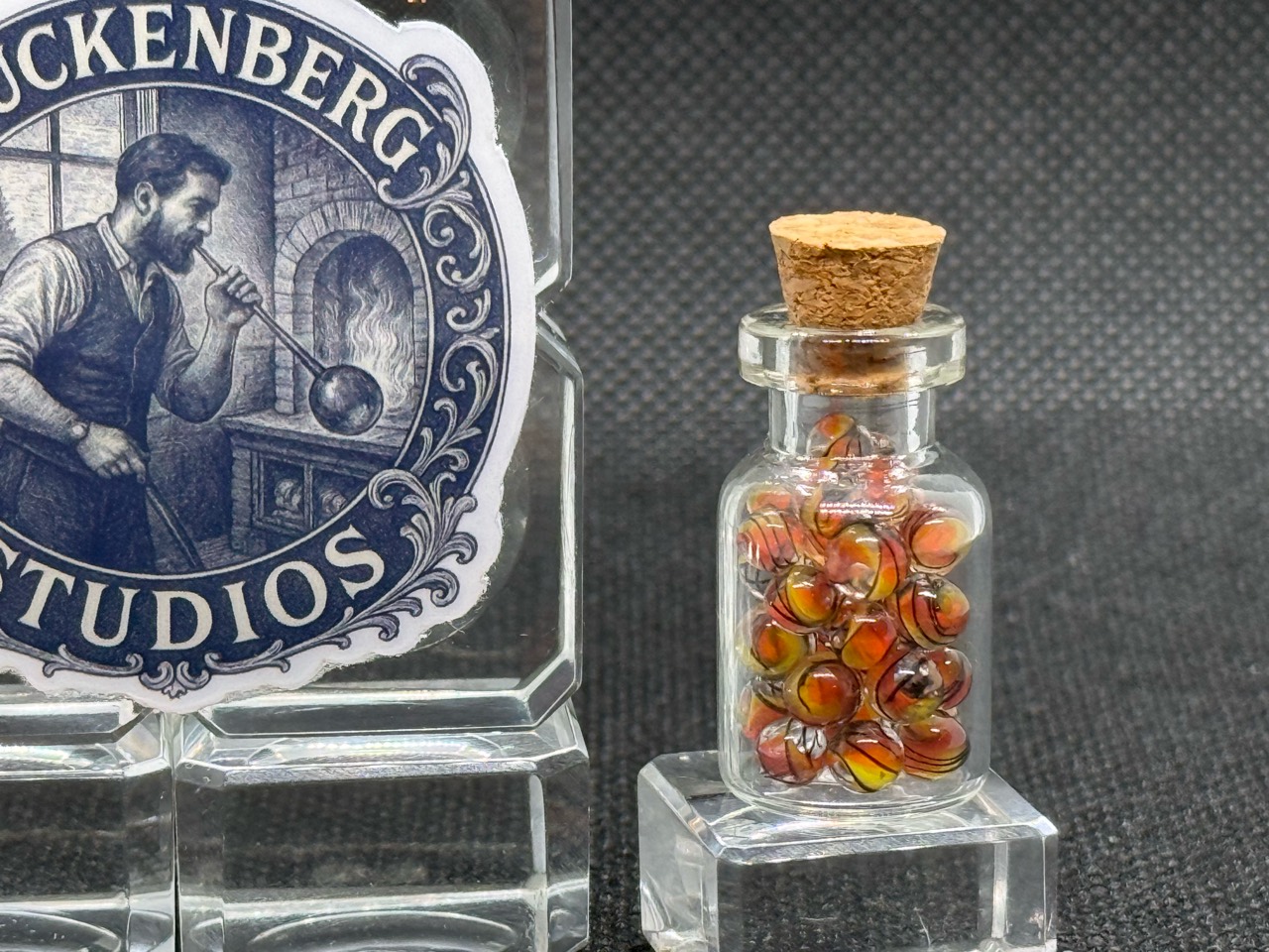 Close view of Fine Line Flame Mini Micro Marbles in their corked jar beside studio branding