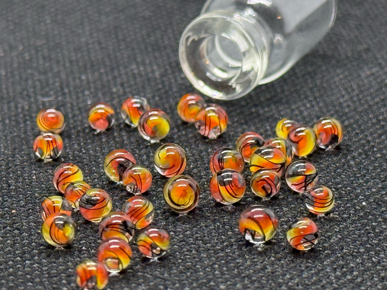Loose Fine Line Flame Mini Micro Marbles with warm yellow, orange and red swirls and fine dark lines beside their open jar