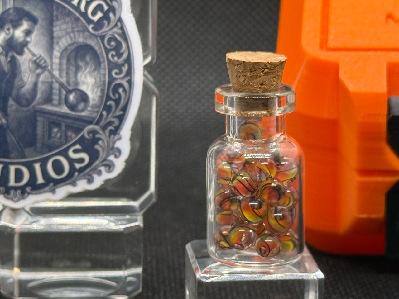 Close view of Fine Line Flame marble jar with fine dark lines across warm colored swirls and an orange case in the background