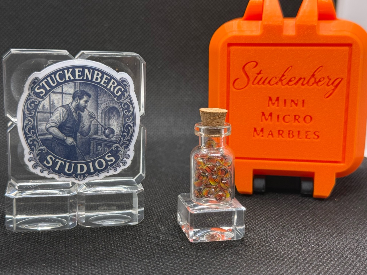 Fine Line Flame Mini Micro Marbles in a corked jar beside studio branding and an upright orange hard case