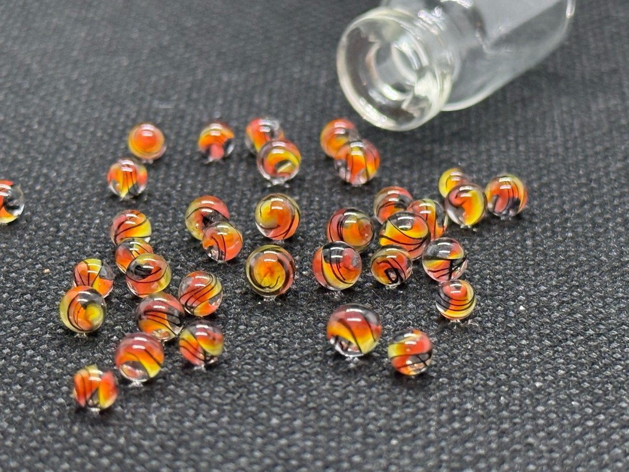 Alternate view of loose Fine Line Flame Mini Micro Marbles beside their open jar