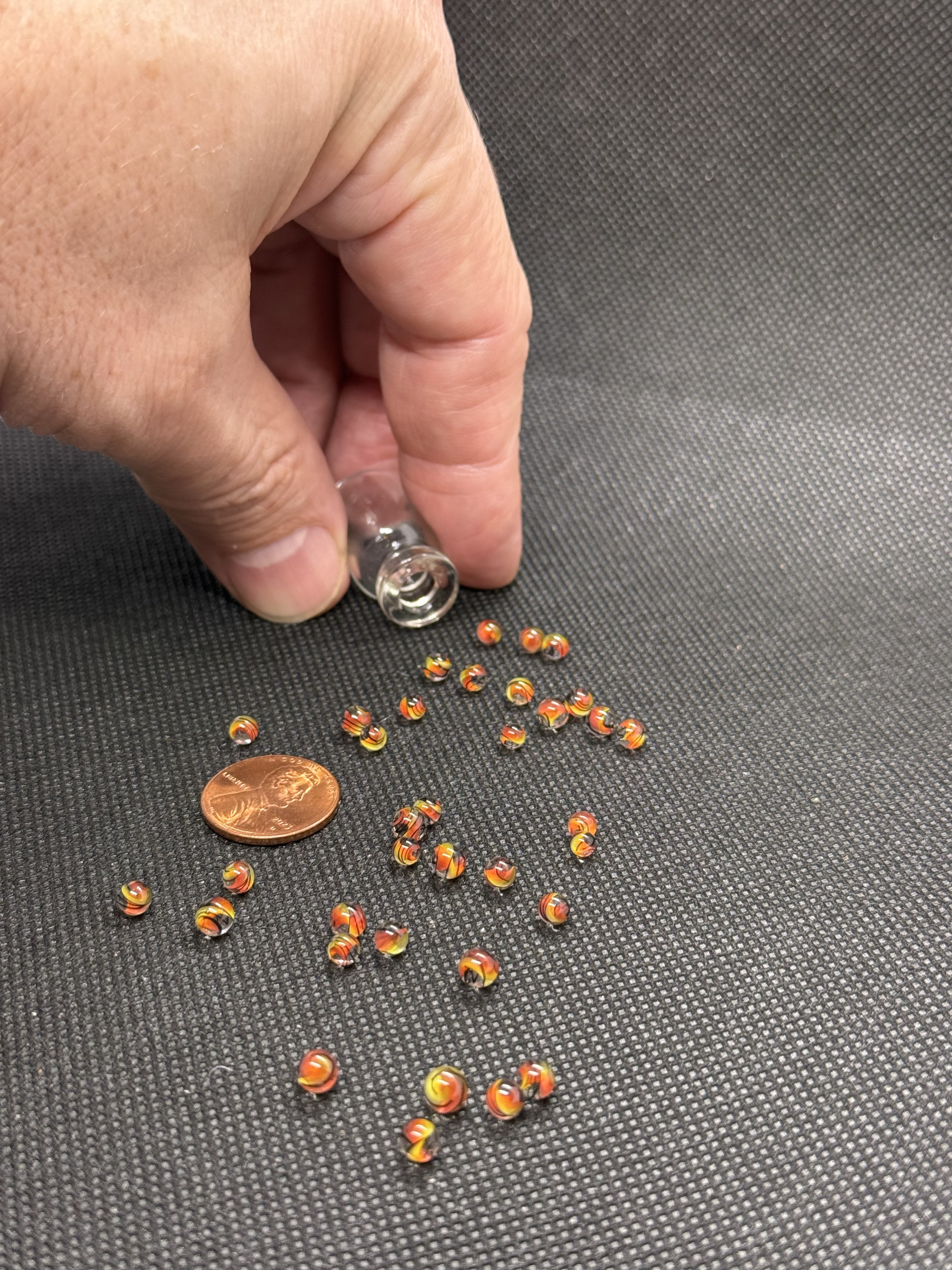 Fine Line Flame Mini Micro Marbles beside a penny and an open jar held in hand for scale