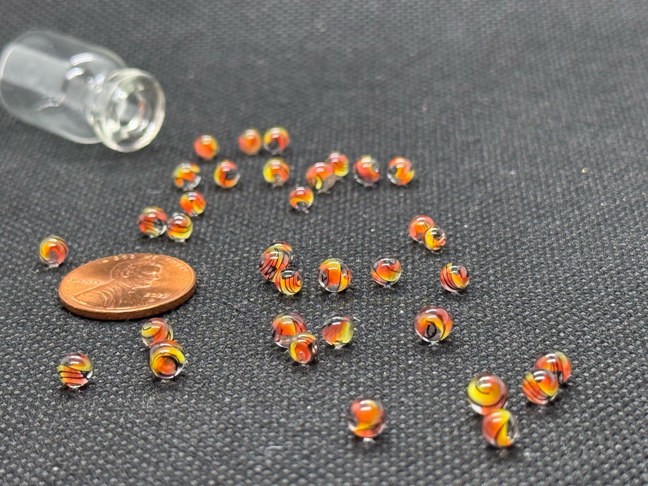 Loose Fine Line Flame Mini Micro Marbles with warm colored swirls and fine dark lines beside a penny for scale