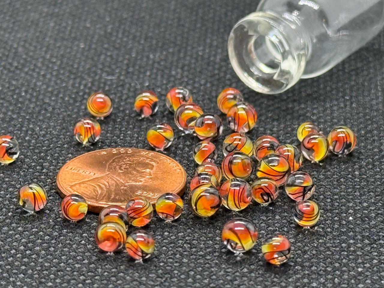Fine Line Flame Mini Micro Marbles around a penny for scale beside their open jar