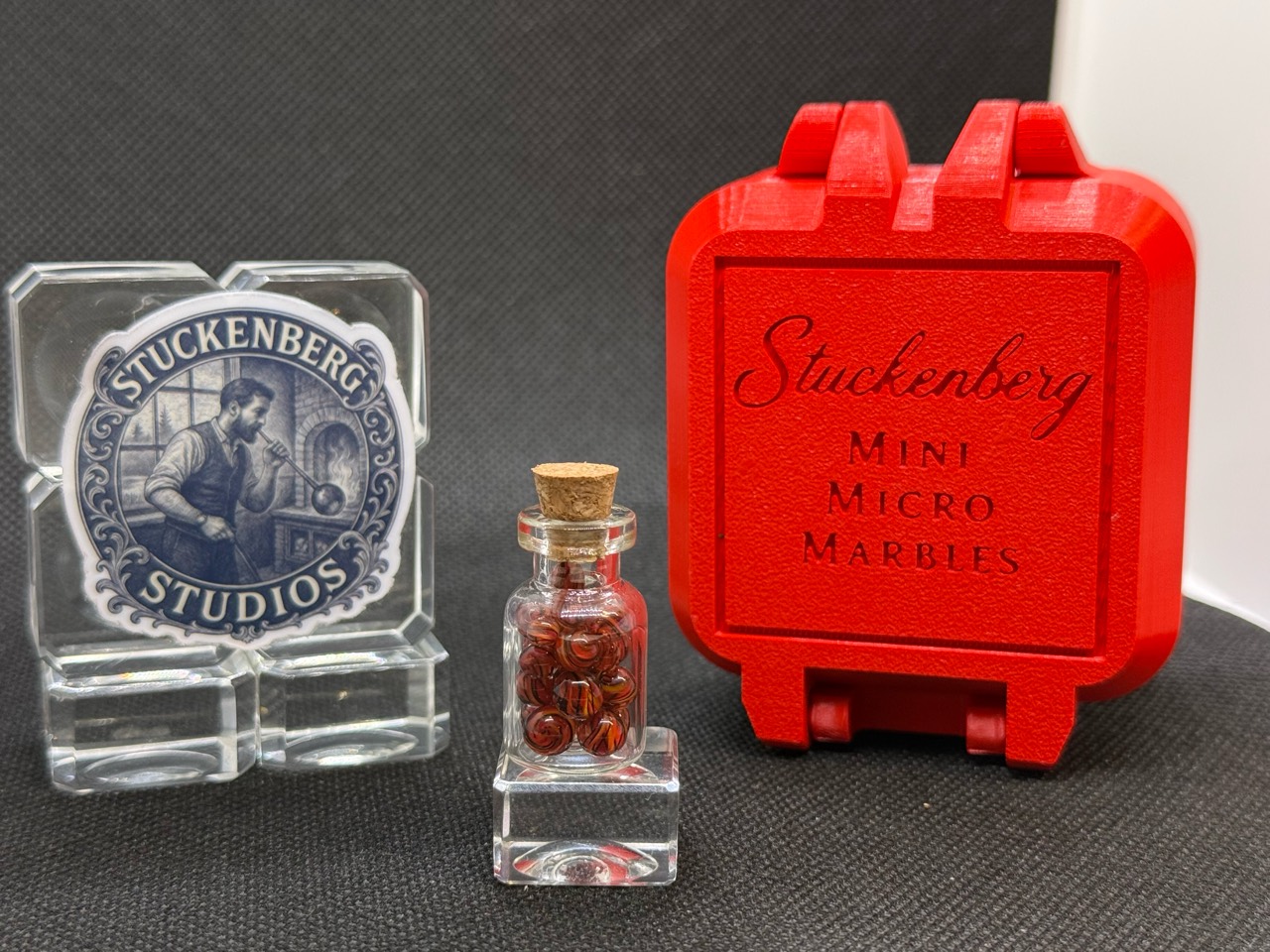 Fire Brick Ribbon Mini Micro Marbles in a corked jar beside the studio display and red hard case