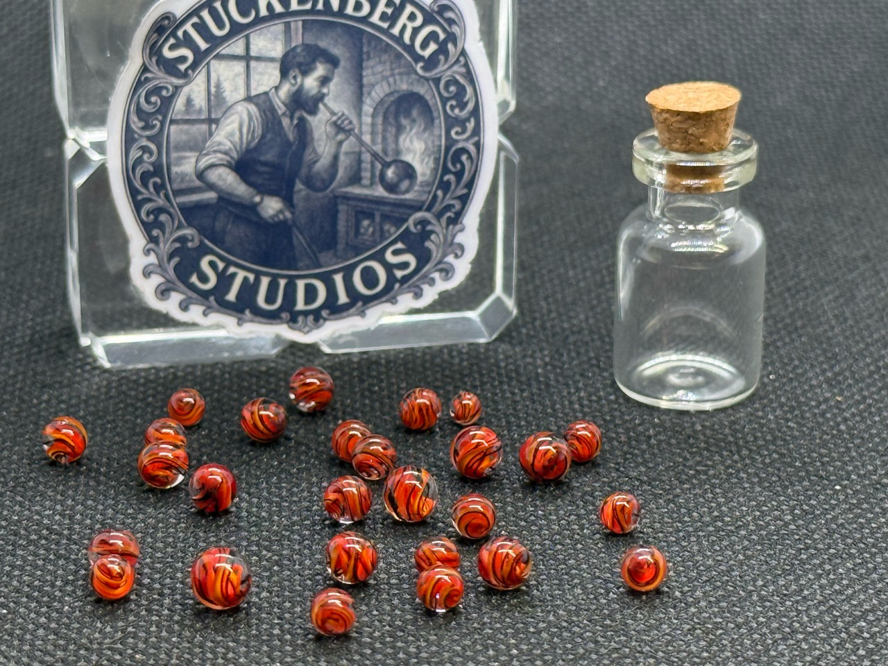 Loose Fire Brick Ribbon Mini Micro Marbles beside their empty jar and studio display