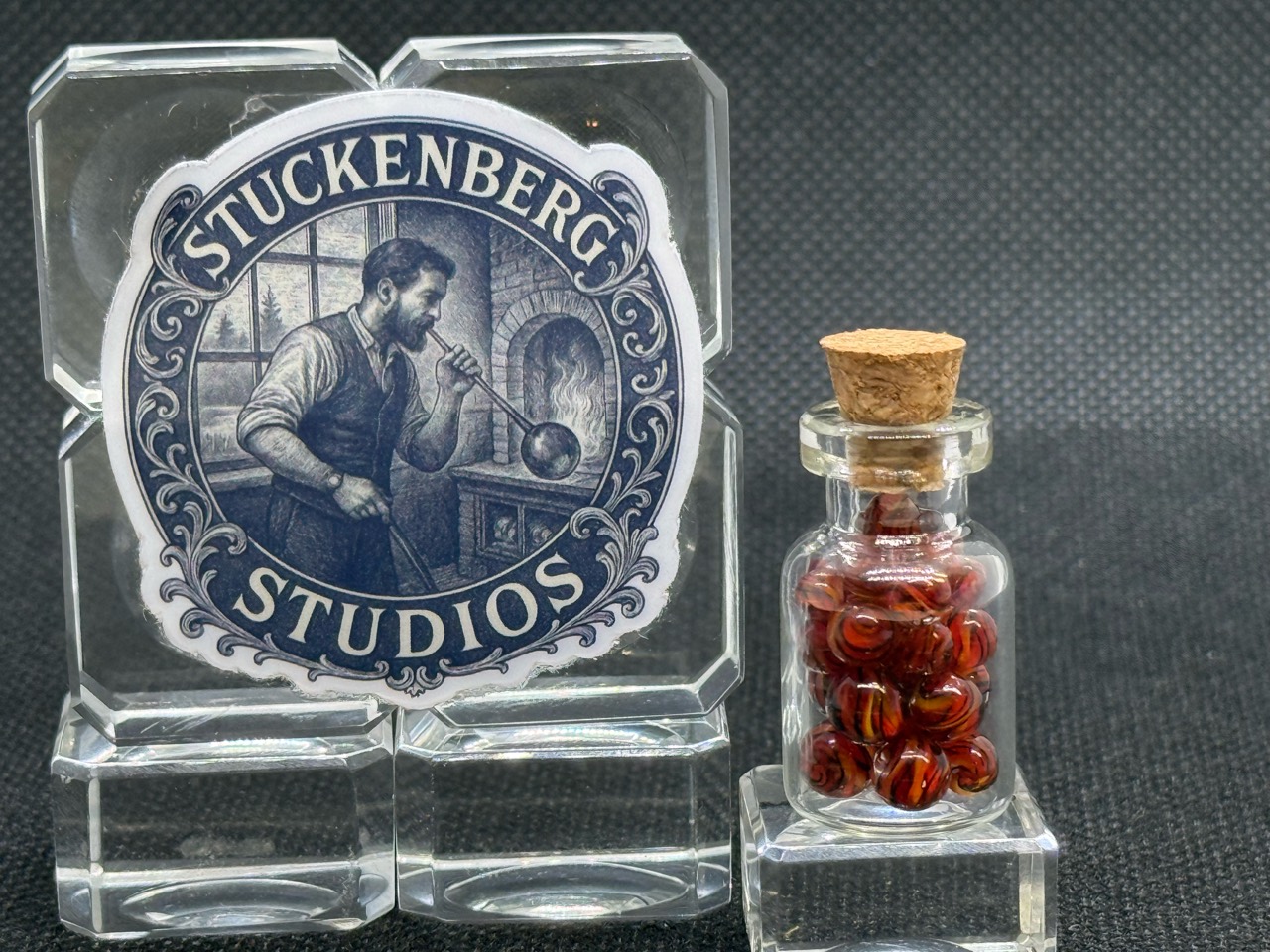 Corked jar of Fire Brick Ribbon Mini Micro Marbles beside the studio display