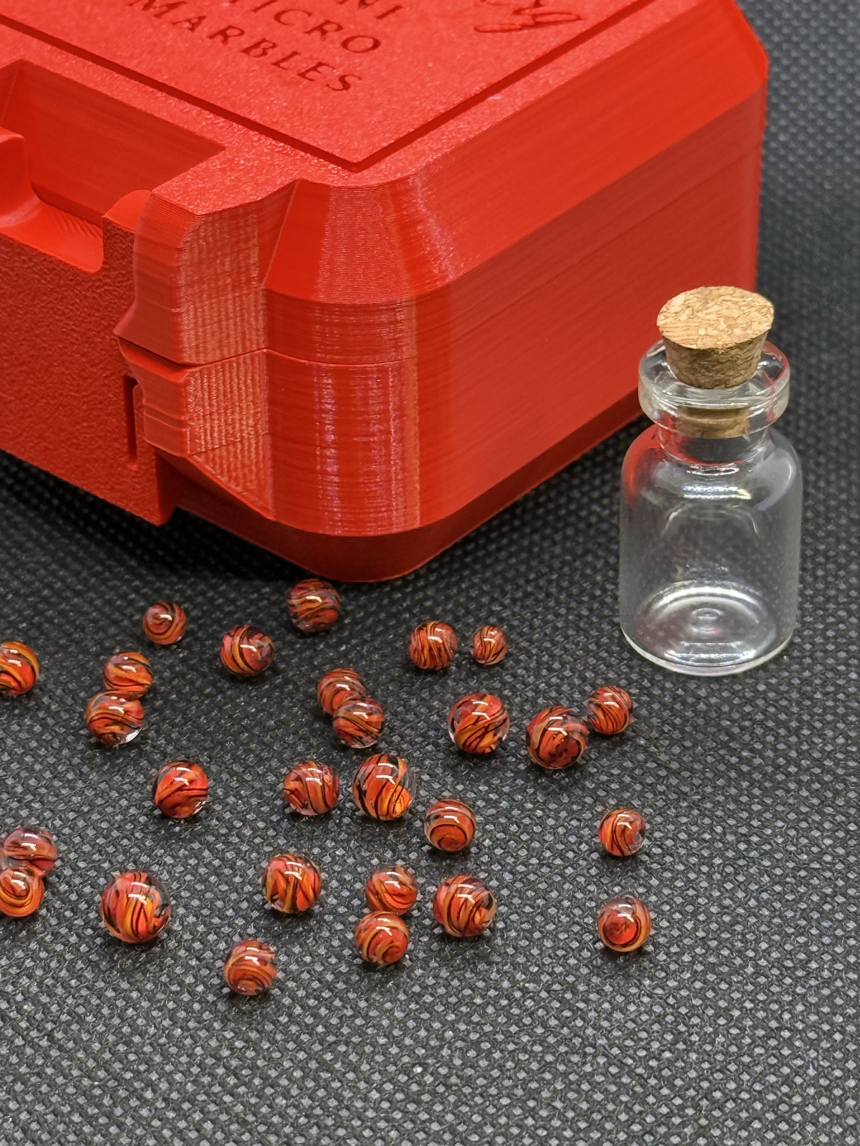 Fire Brick Ribbon Mini Micro Marbles beside the red hard case and empty jar