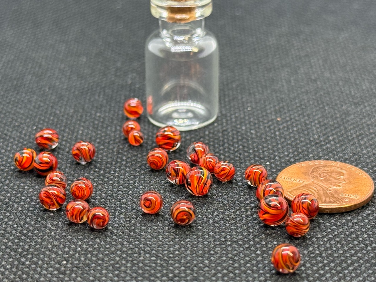 Fire Brick Ribbon Mini Micro Marbles beside a penny and empty jar for scale