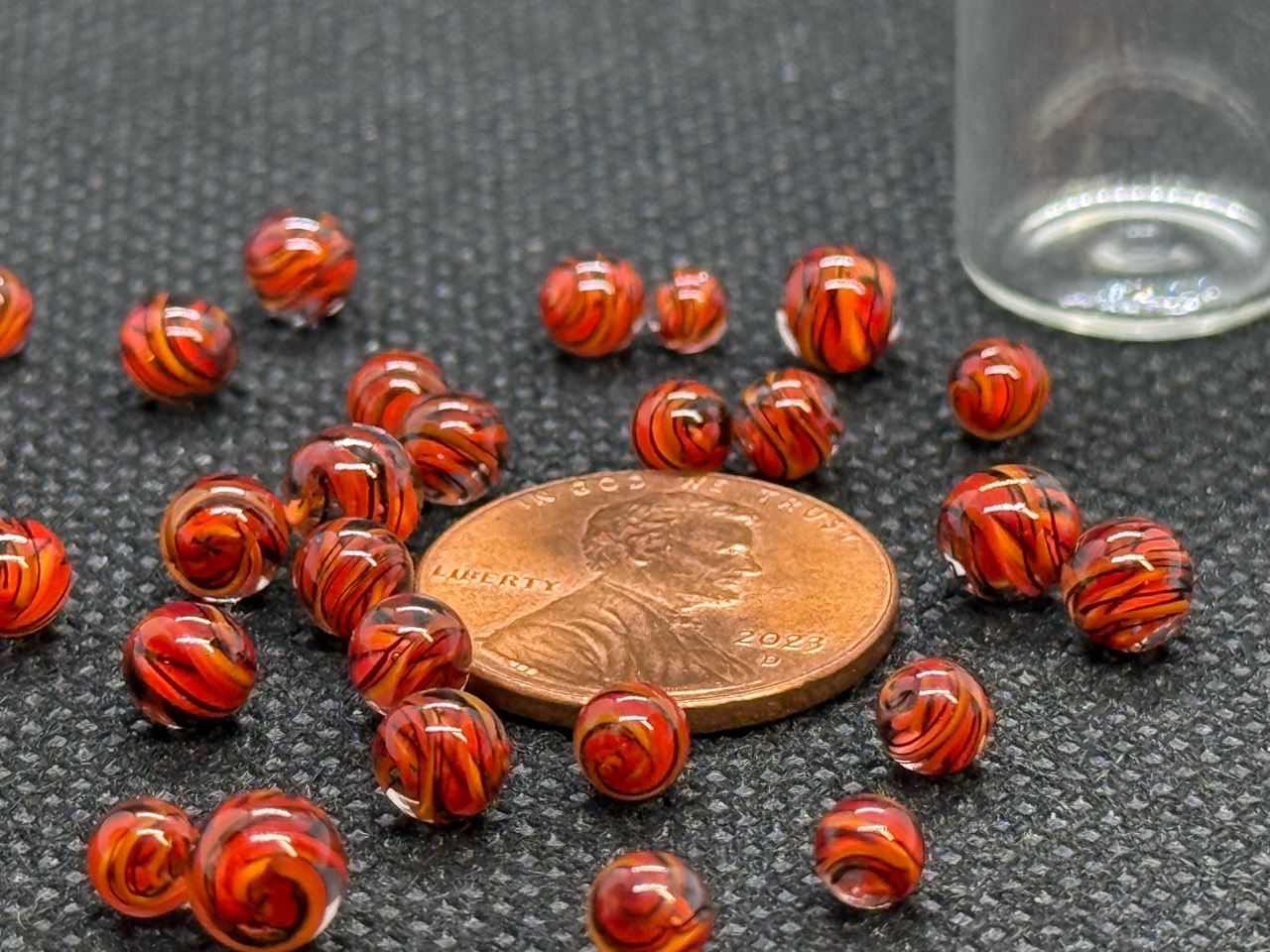 Fire Brick Ribbon Mini Micro Marbles gathered around a penny for scale