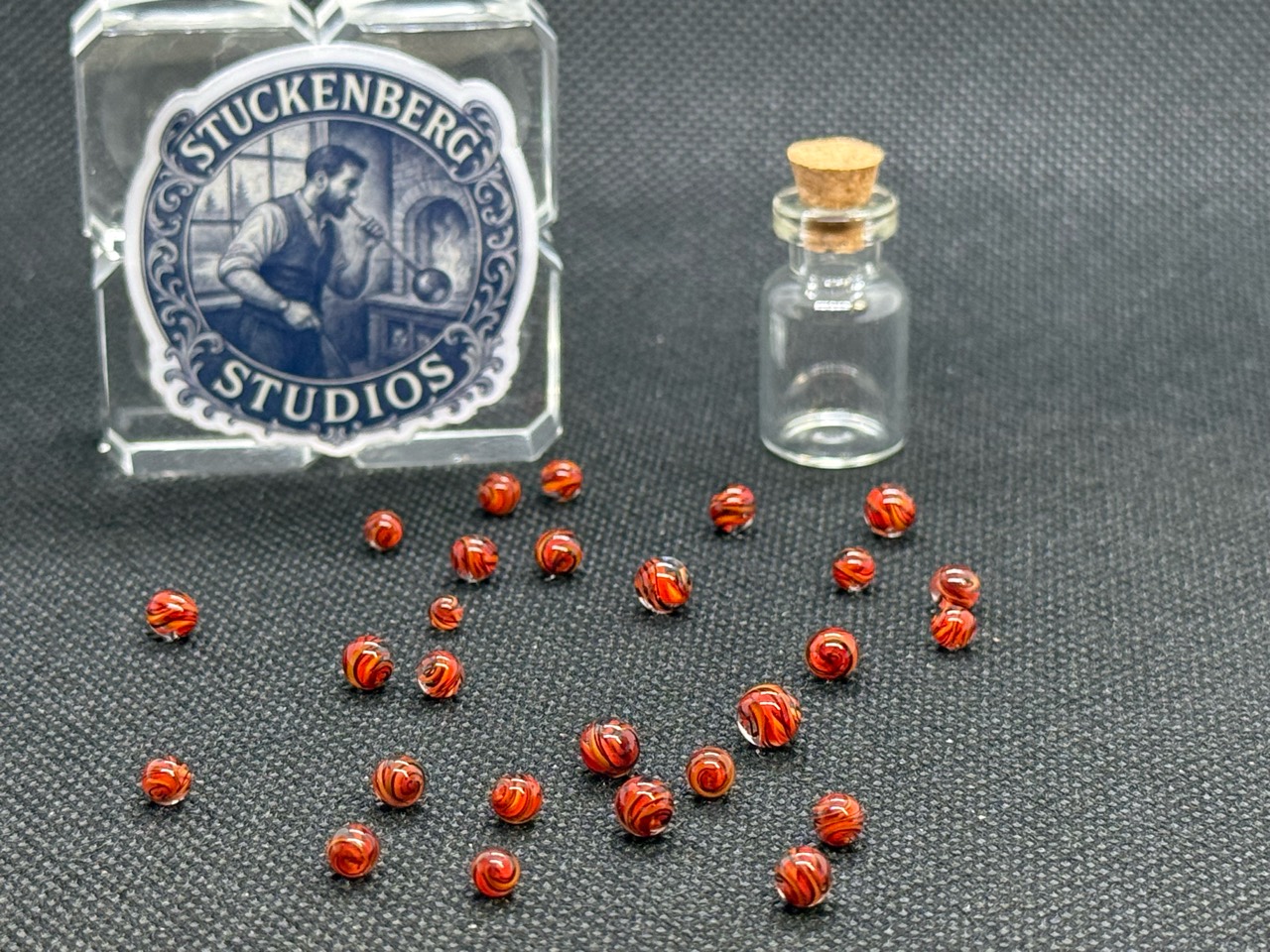 Wide view of Fire Brick Ribbon Mini Micro Marbles with their empty jar and studio display