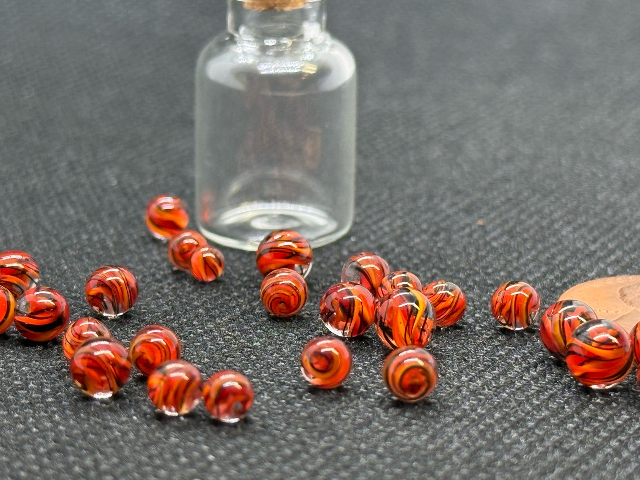 Close view of Fire Brick Ribbon Mini Micro Marbles beside a penny and empty jar for scale