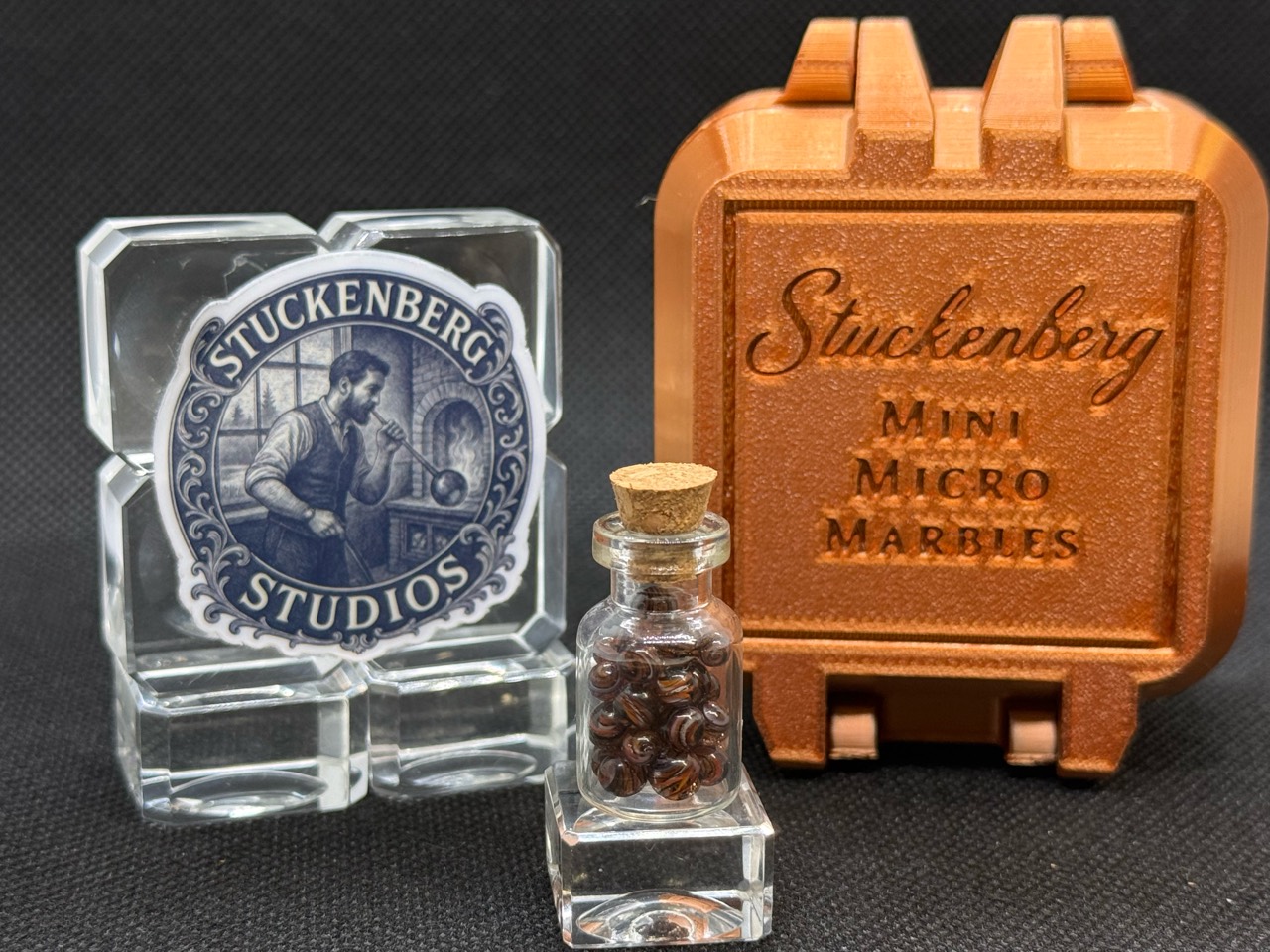 Goldstone Mini Micro Marbles in a corked glass jar beside studio branding and a copper-colored display case