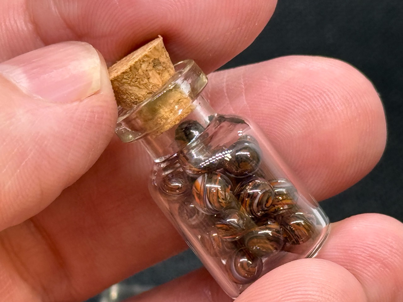 Corked jar of Goldstone Mini Micro Marbles held between fingers for scale