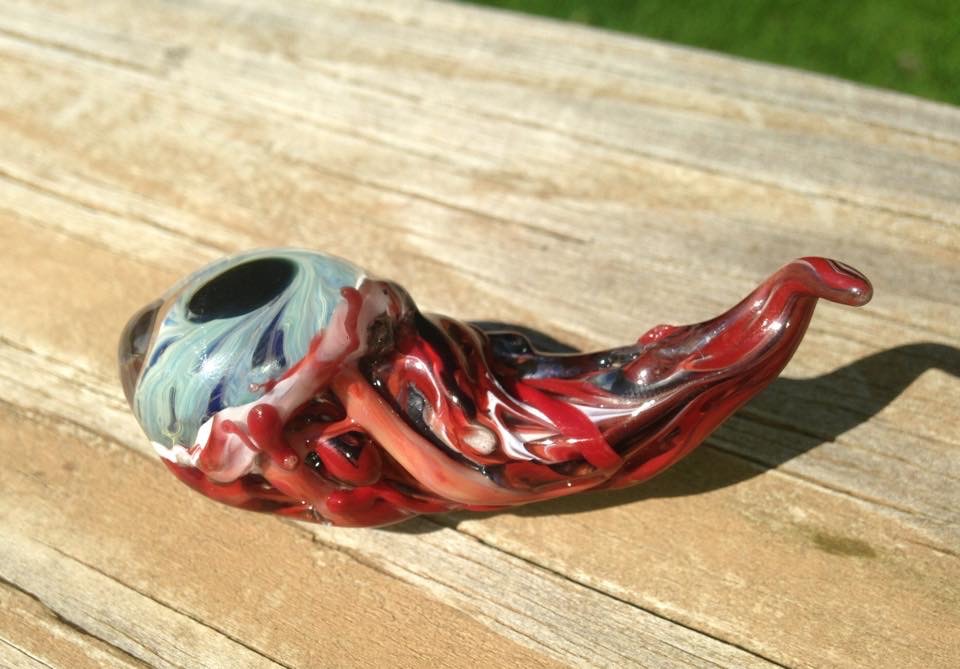 Halloween Zombie Eyeballs: Sunlit side view of a pale blue glass zombie eye with curling red and dark tendrils on a wooden surface